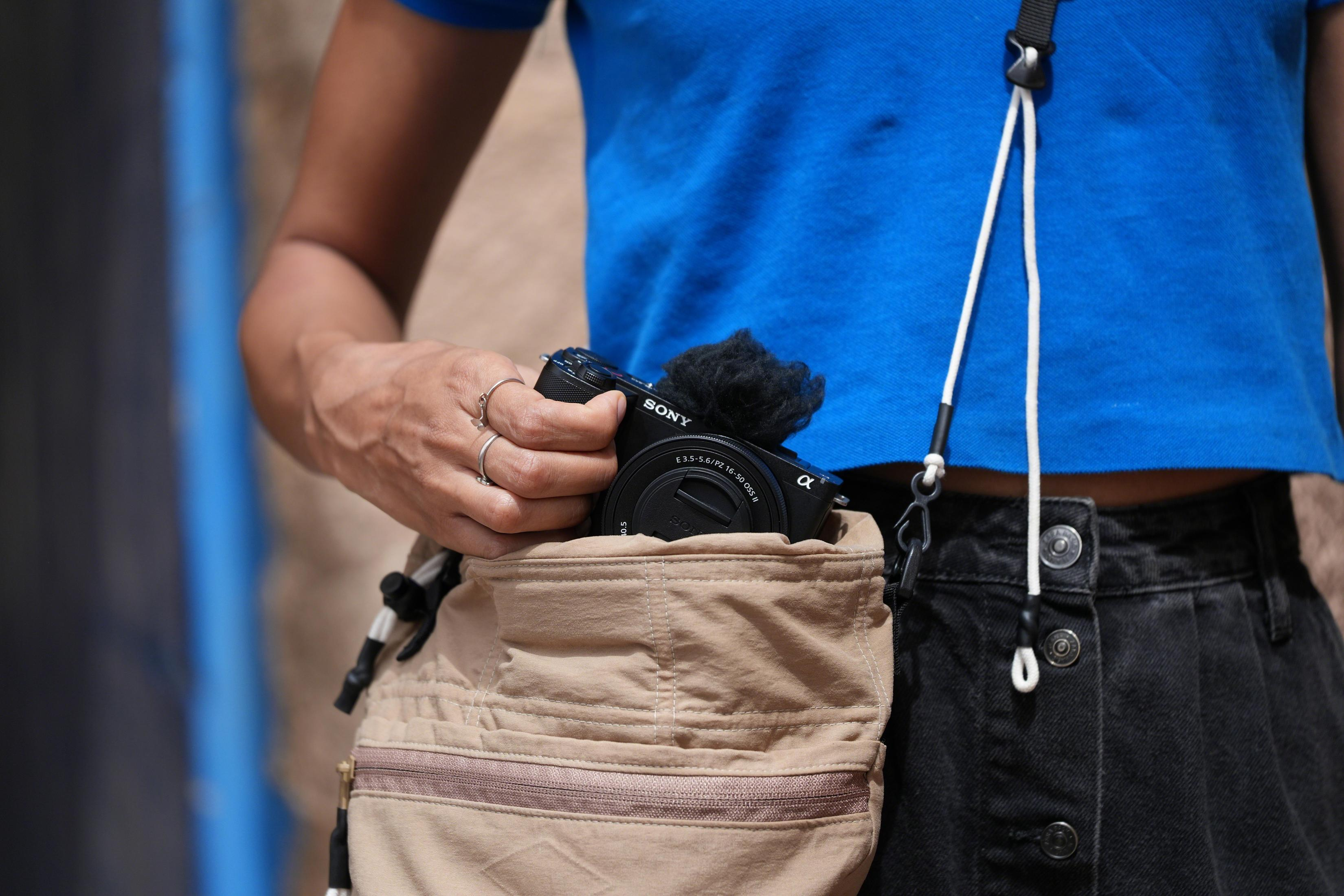Una persona con top blu e gonna nera mette una fotocamera Sony in una borsa.