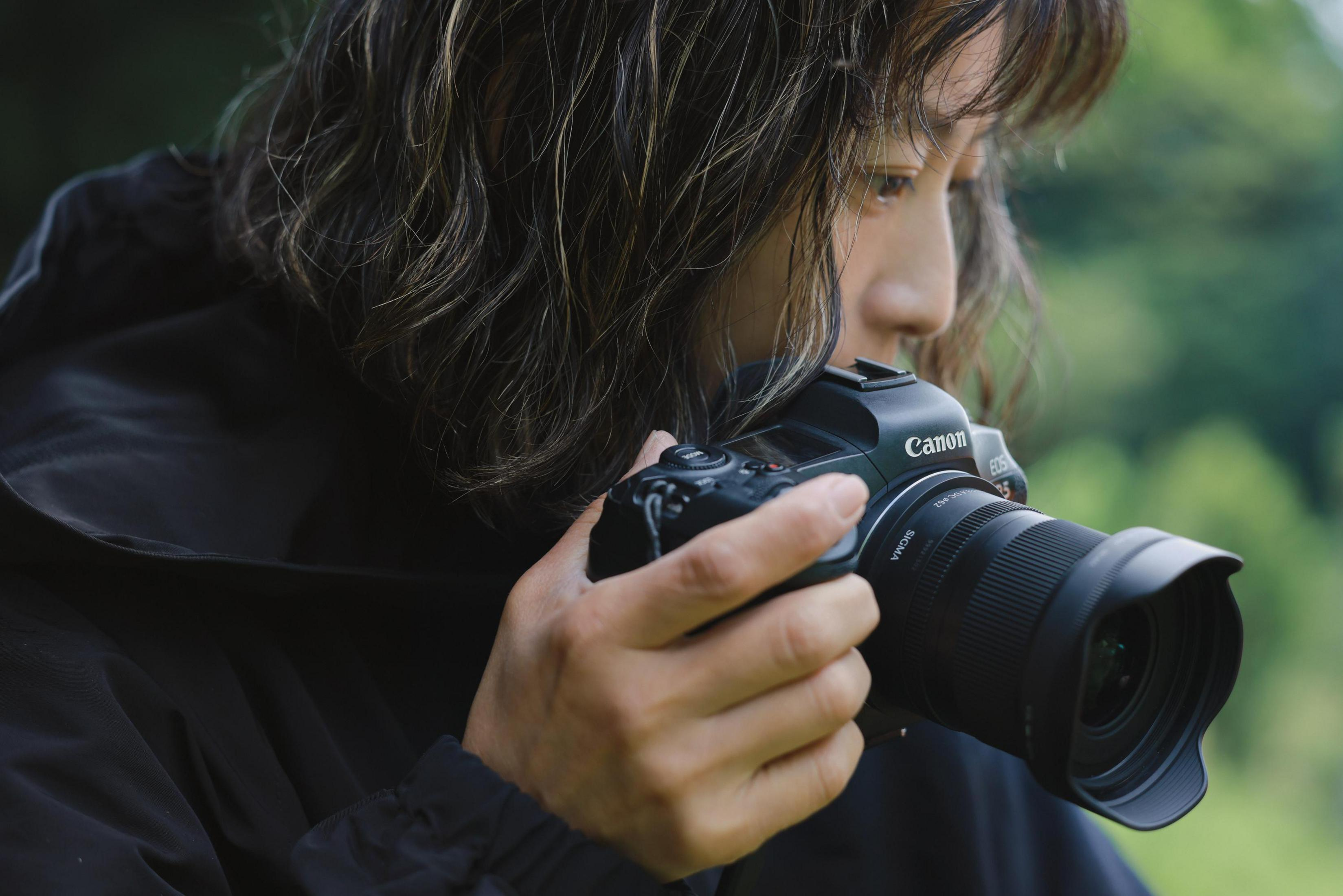 Eine Person hält eine schwarze Canon EOS R5 Kamera mit einem Sigma Objektiv.