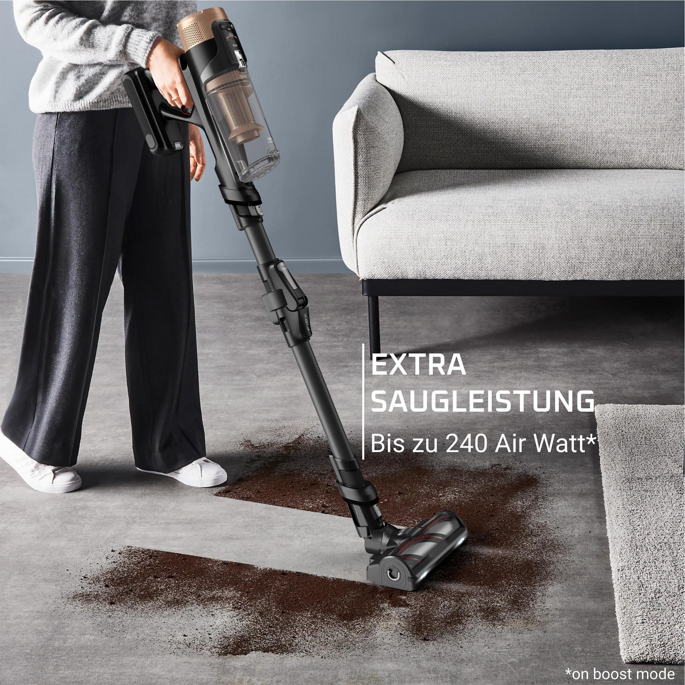 Person saugt braunen Staub auf Betonboden neben Sofa.