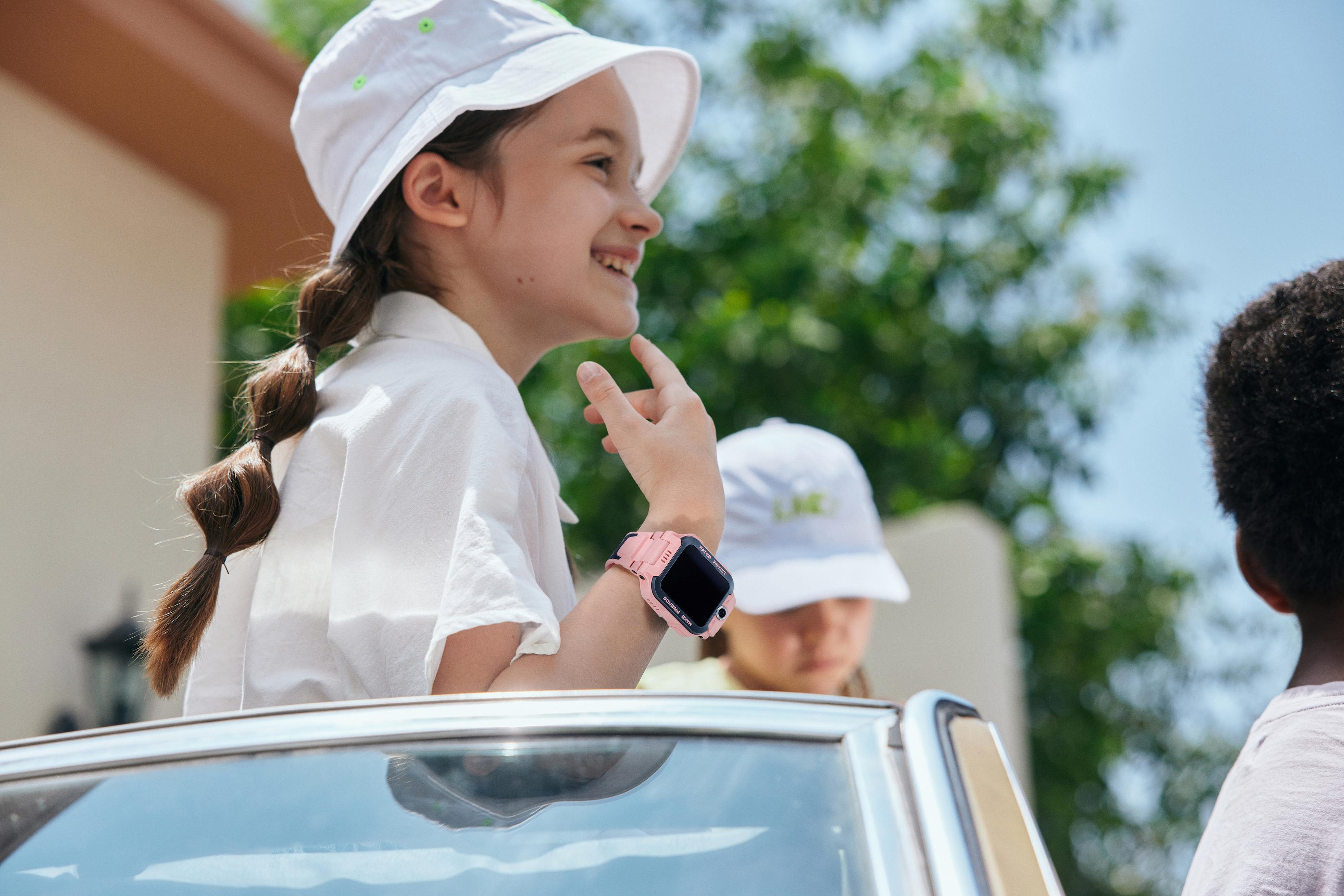 Una ragazza con uno smartwatch rosa e un ragazzo in macchina. Alberi verdi.