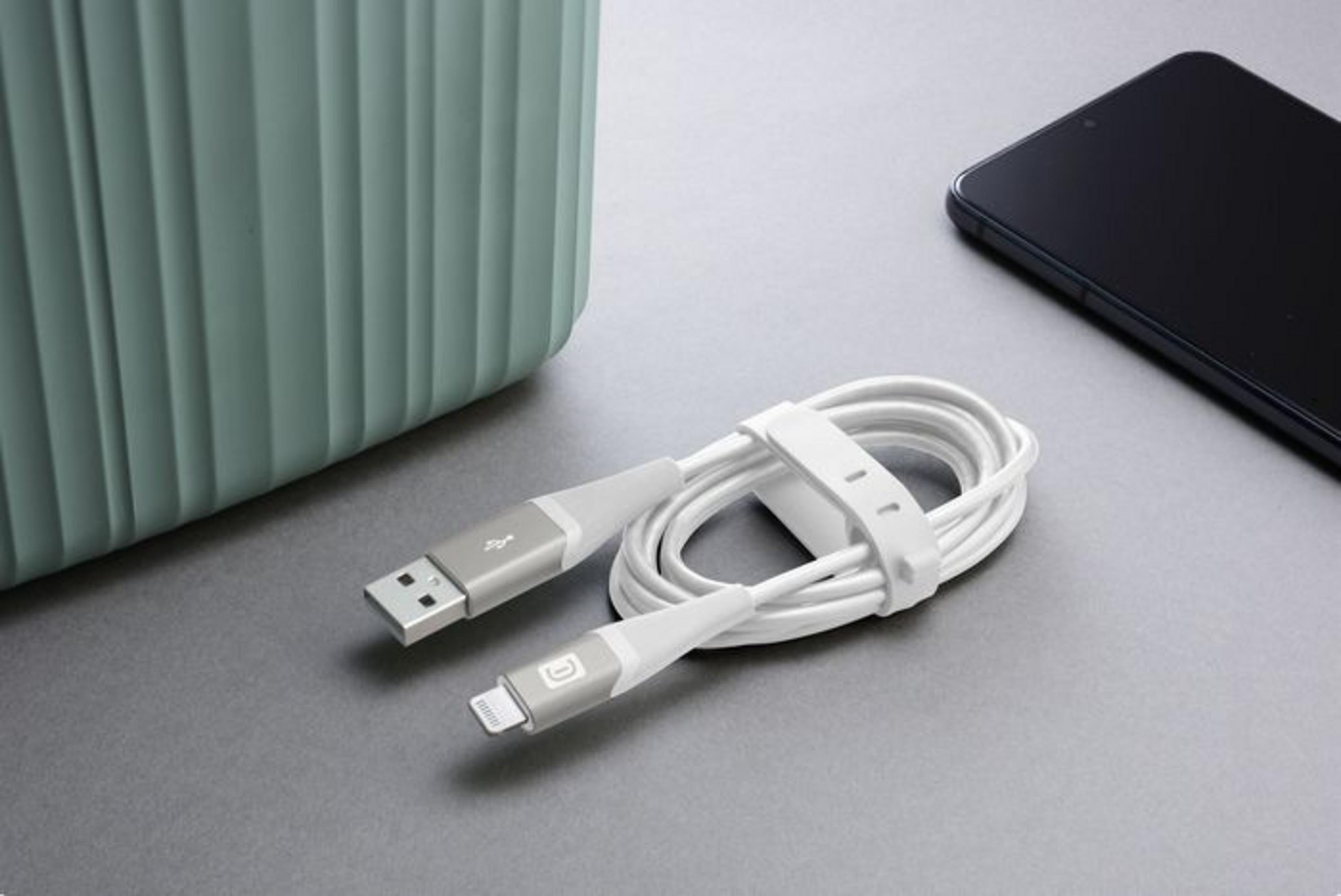 Un cavo di ricarica bianco giace accanto a uno smartphone e un contenitore verde.