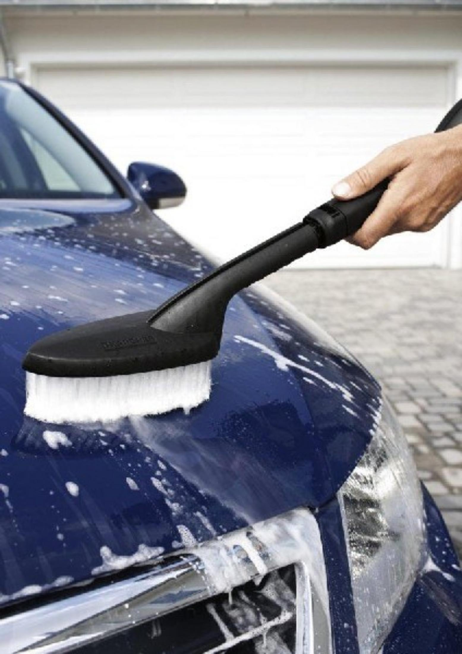 Una mano sostiene un cepillo que limpia una superficie de coche azul y mojada.