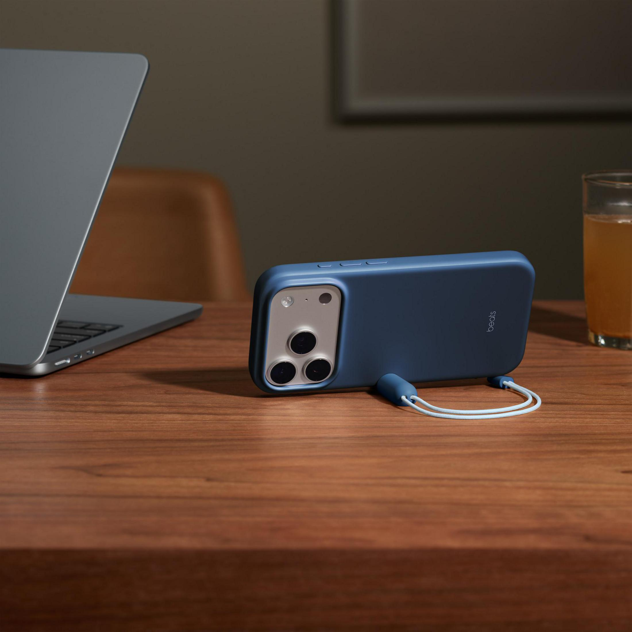 Blaues Handy mit Lanyard liegt auf einem Holztisch neben einem Laptop und Glas.