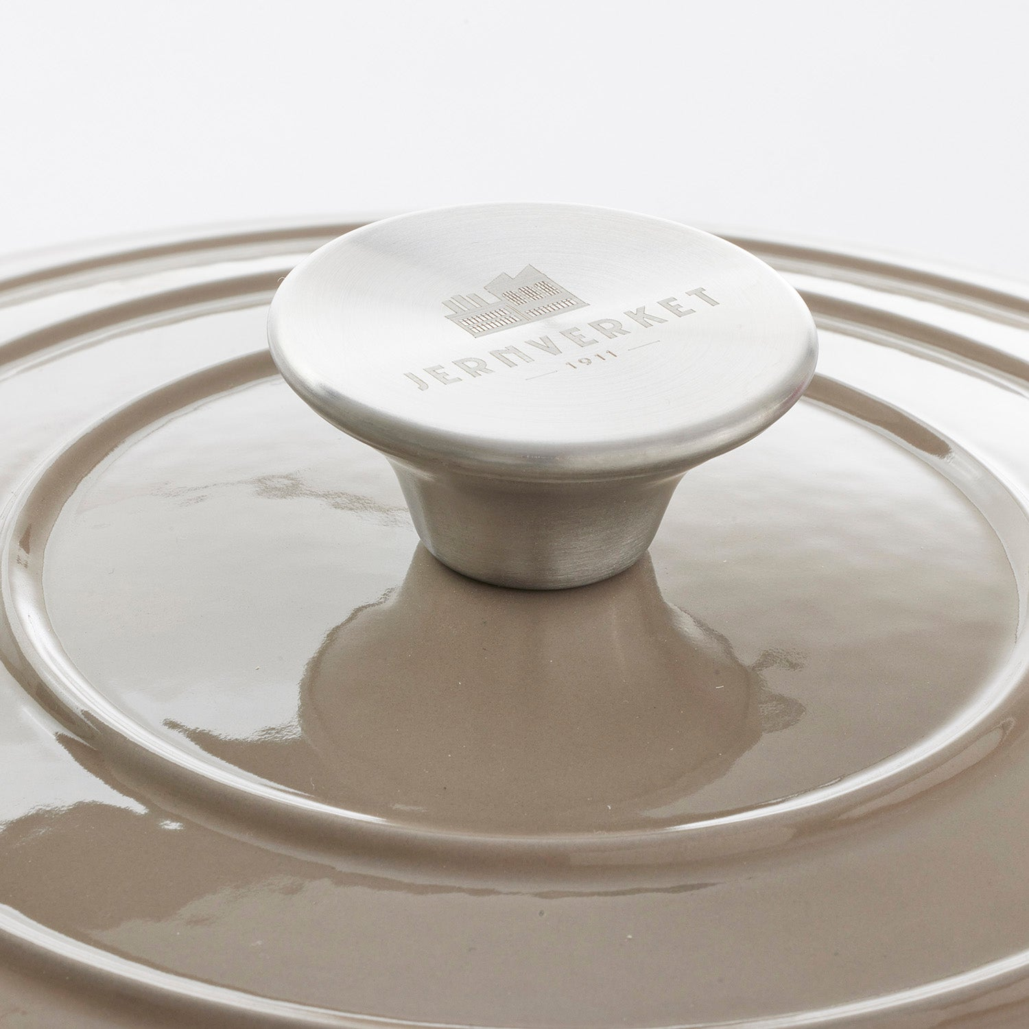 Tapa de olla gris con asa plateada y letras de marca.