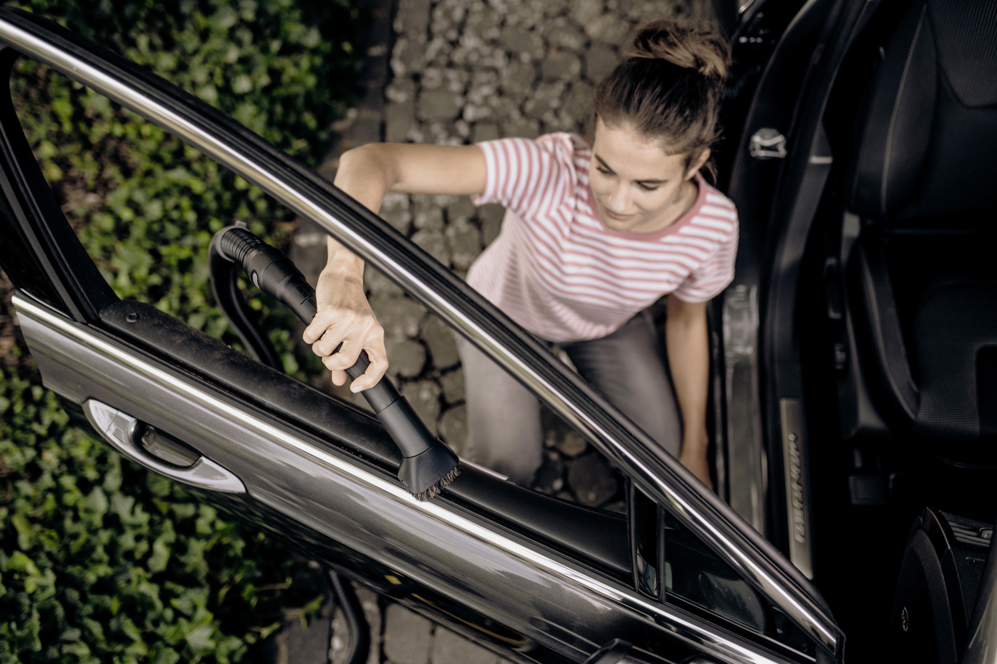 Una donna aspira l'interno di un'auto. Sta usando un accessorio a tubo.