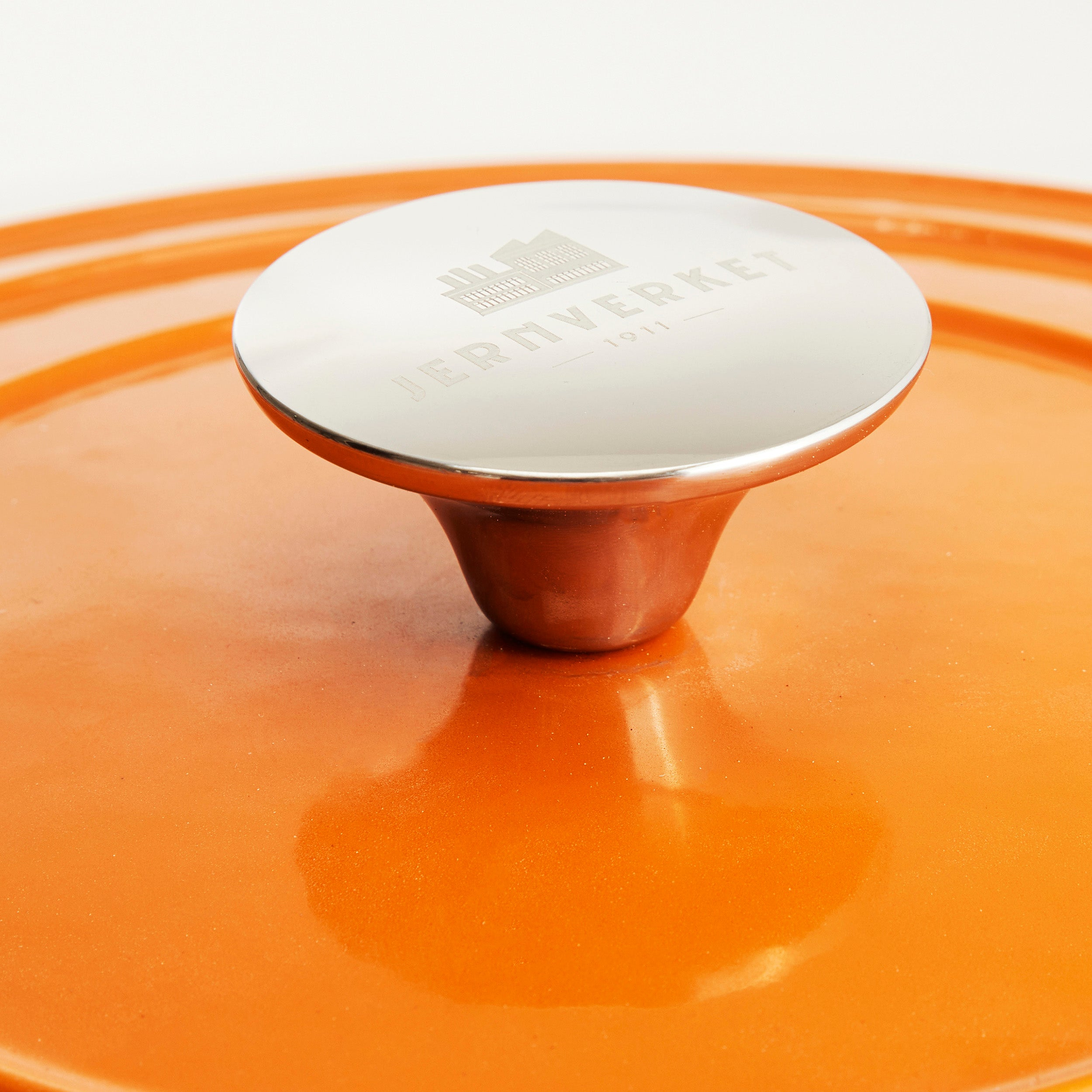 Tapa de olla naranja con asa y logo plateados.