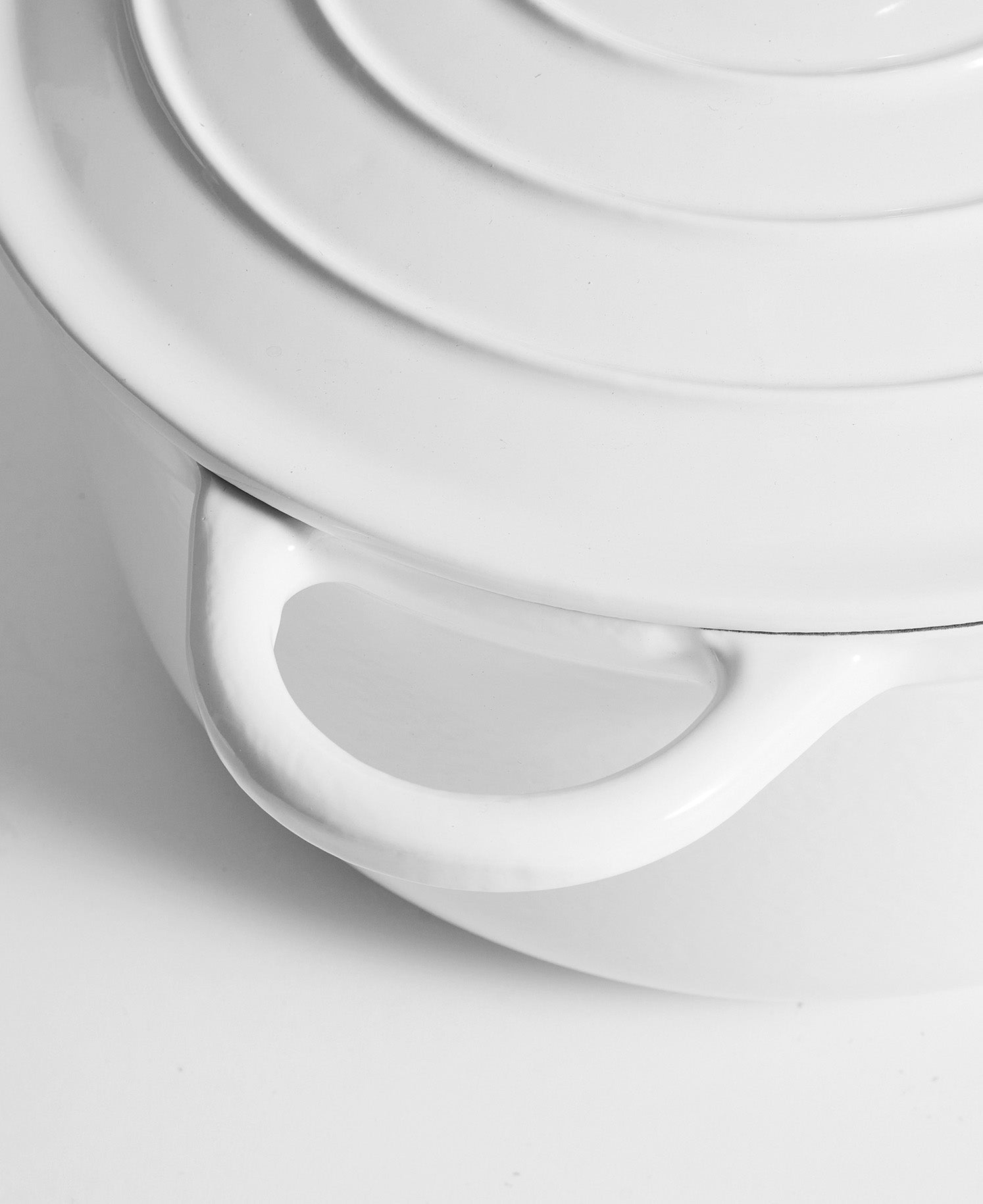 Primer plano de una olla de hierro fundido blanca con anillos concéntricos en la tapa y asa.