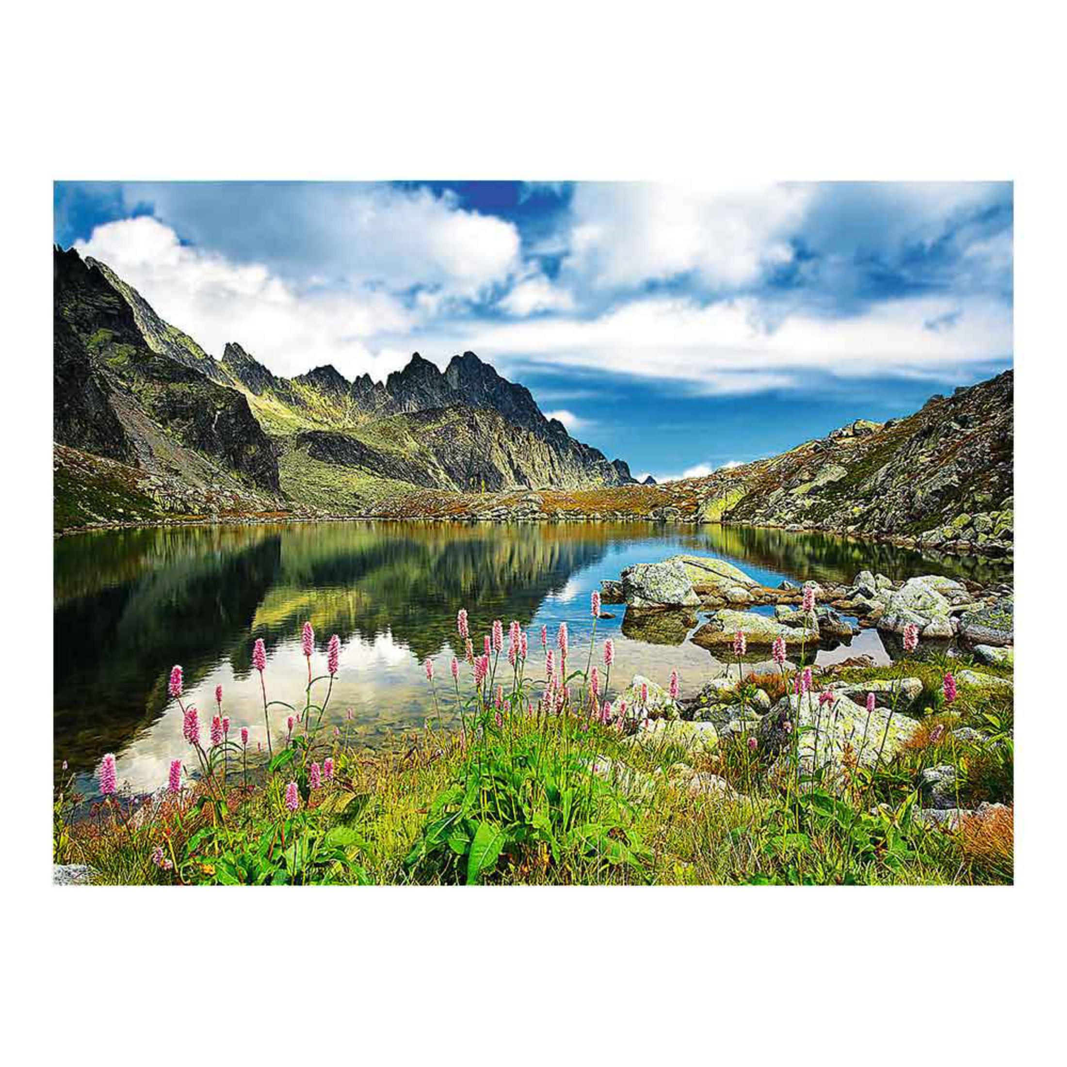 Un lago de montaña con montañas detrás y flores rosas delante.
