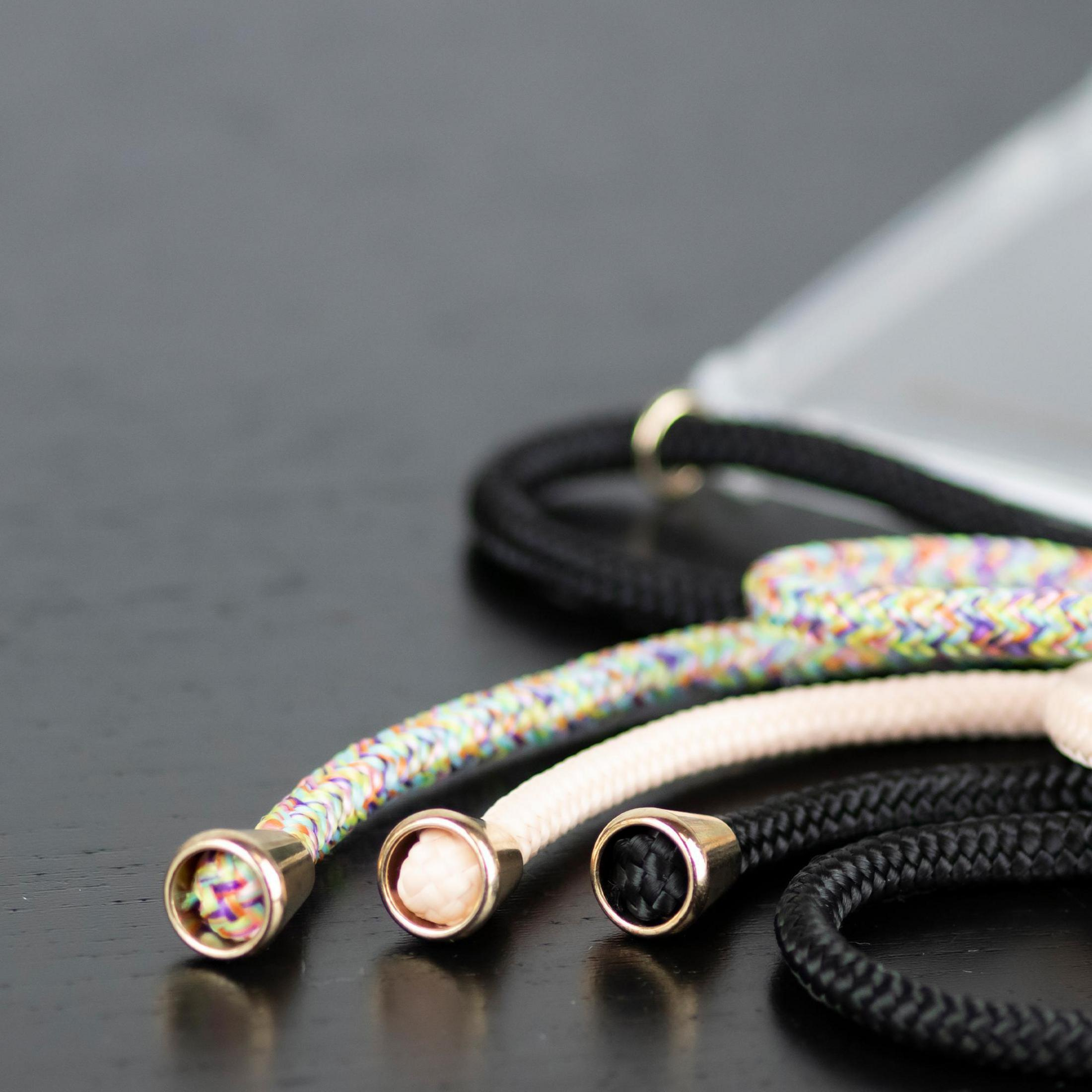 Drei geflochtene Lanyards mit goldenen Spitzen in Schwarz, Creme und Regenbogenfarben.