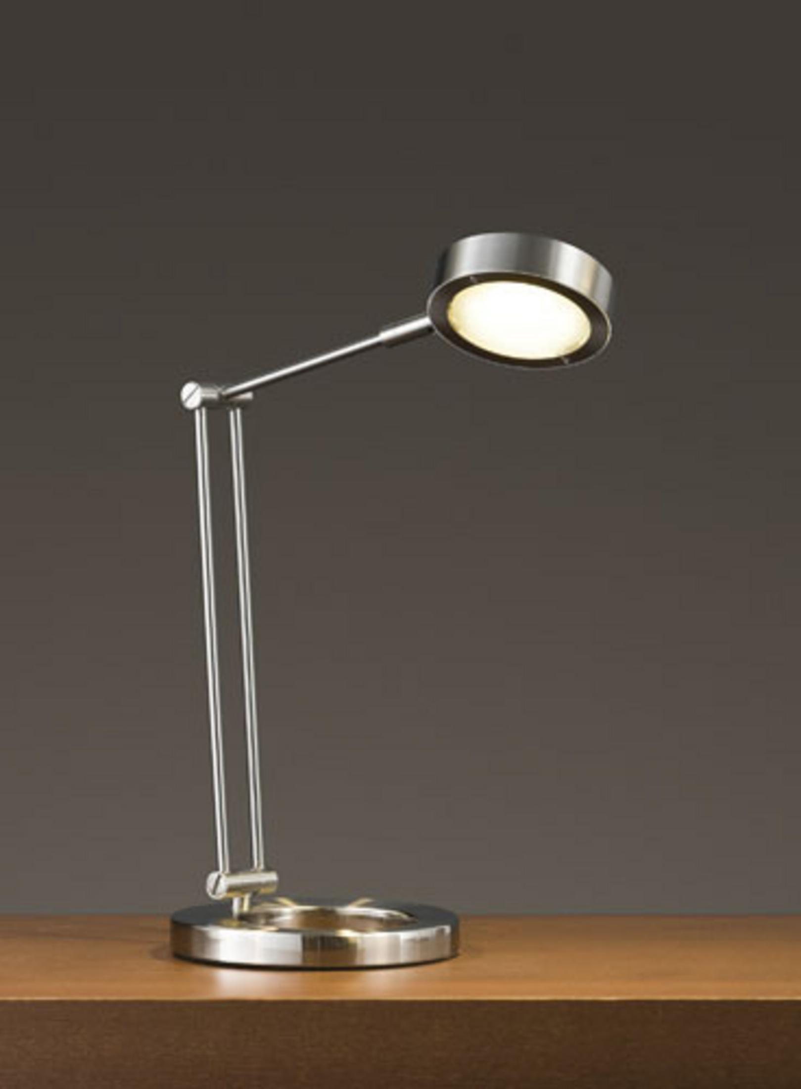 Una moderna lampada da scrivania in argento con braccio regolabile e testa luminosa rotonda su una scrivania in legno.