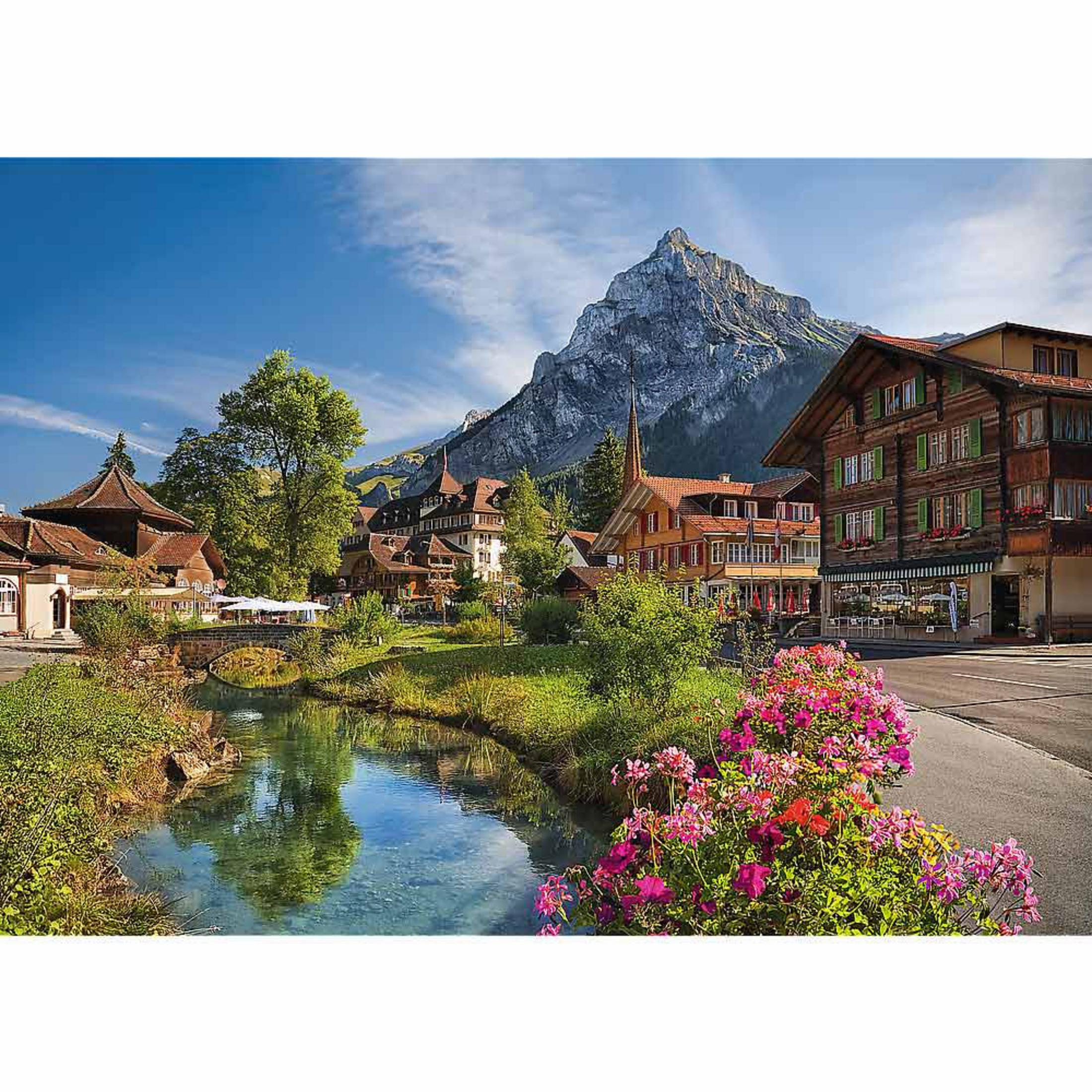 Ein Bergdorf mit Holzhäusern und einem Bach im Vordergrund, dahinter ein hoher Berg.