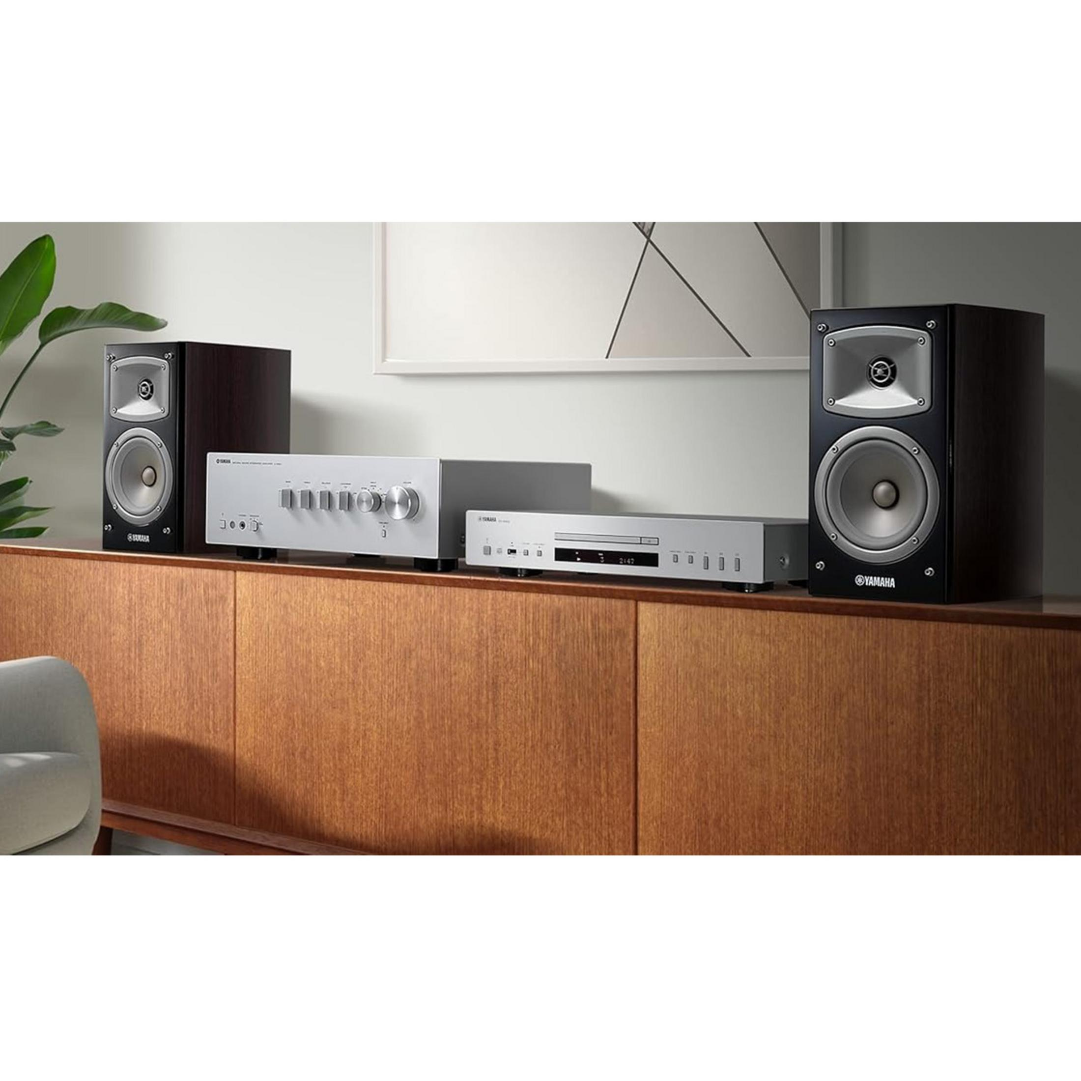 Zwei schwarze Yamaha-Lautsprecher stehen neben einem silbernen CD-Player und Verstärker auf einem Holzschrank.