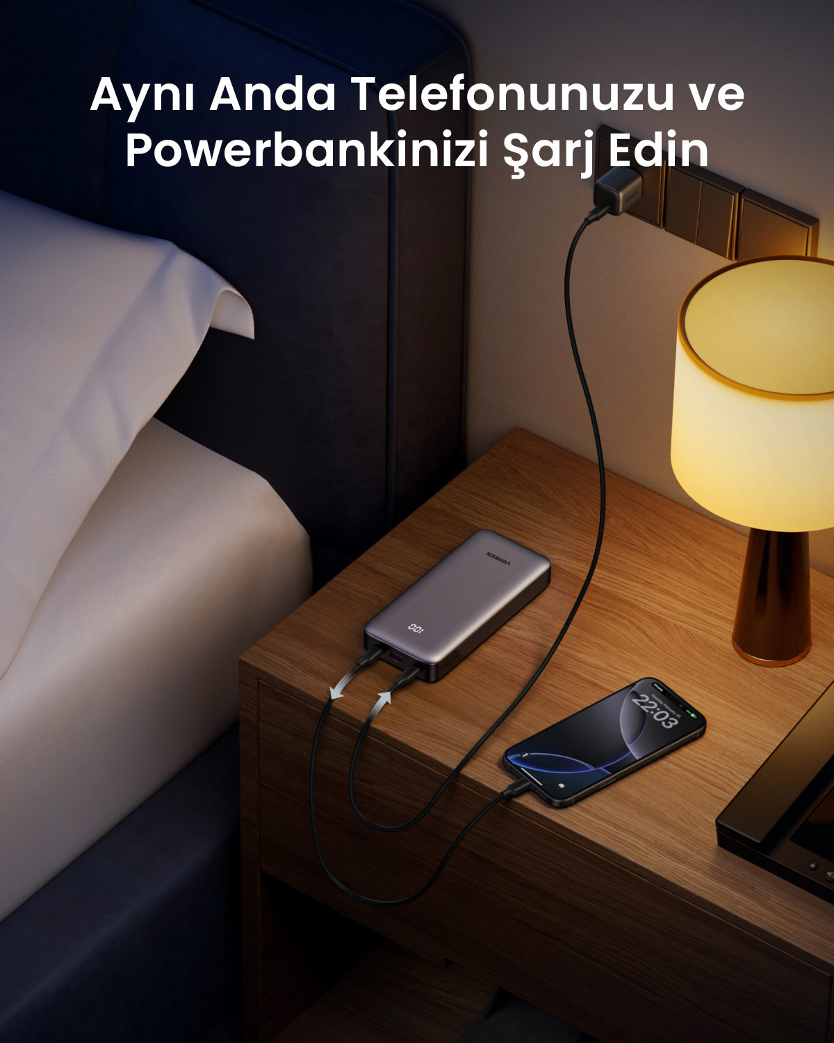 Szary power bank ładuje smartfon na stoliku nocnym.