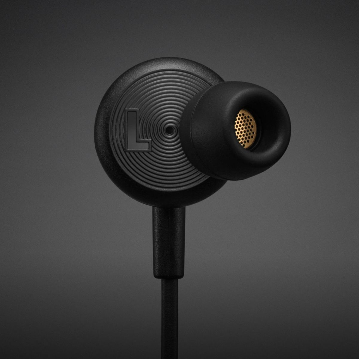 Auricolare nero con griglia dorata, contrassegnato 'L'. Primo piano su sfondo grigio.