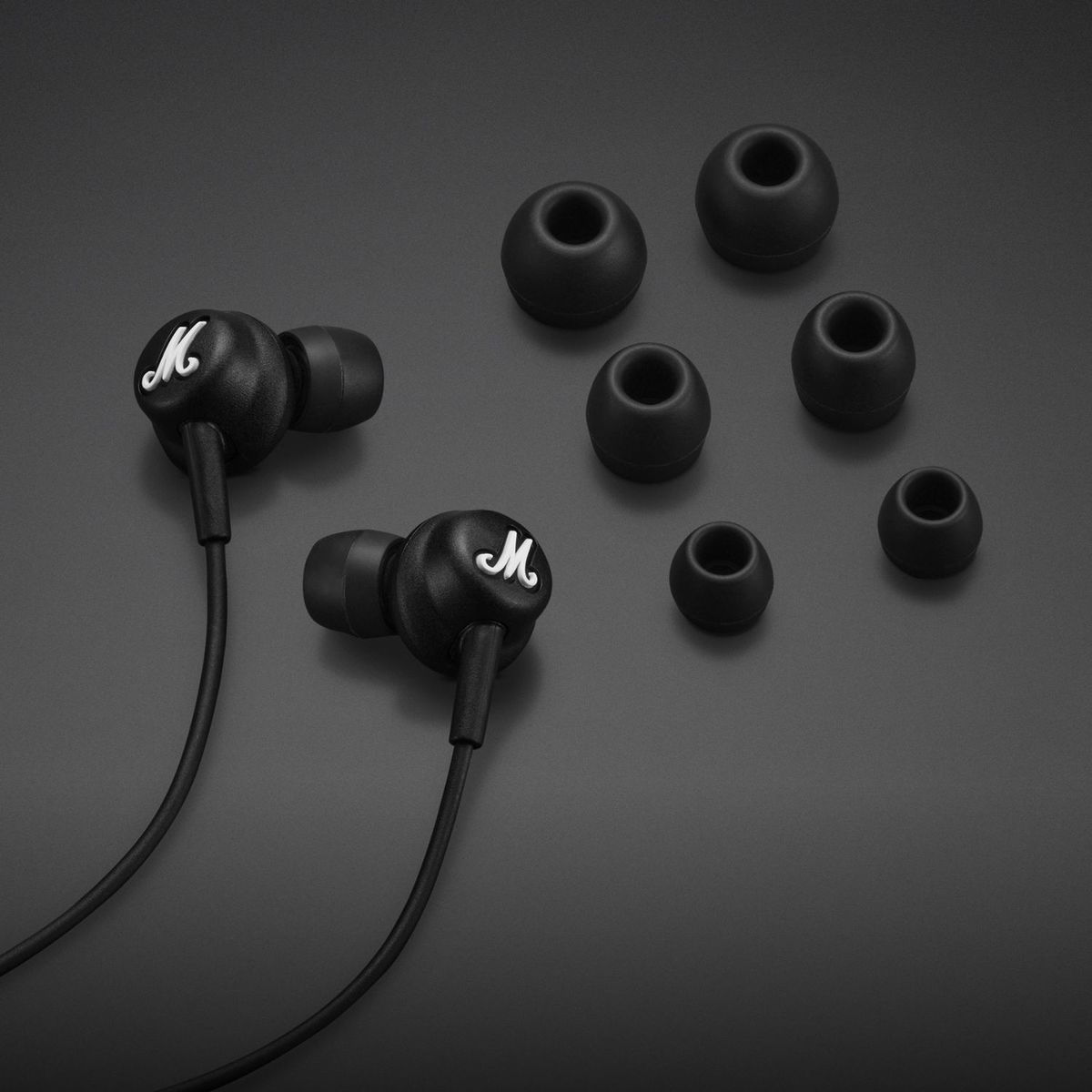 Auricolari Marshall neri con diverse punte auricolari nere su sfondo grigio scuro.