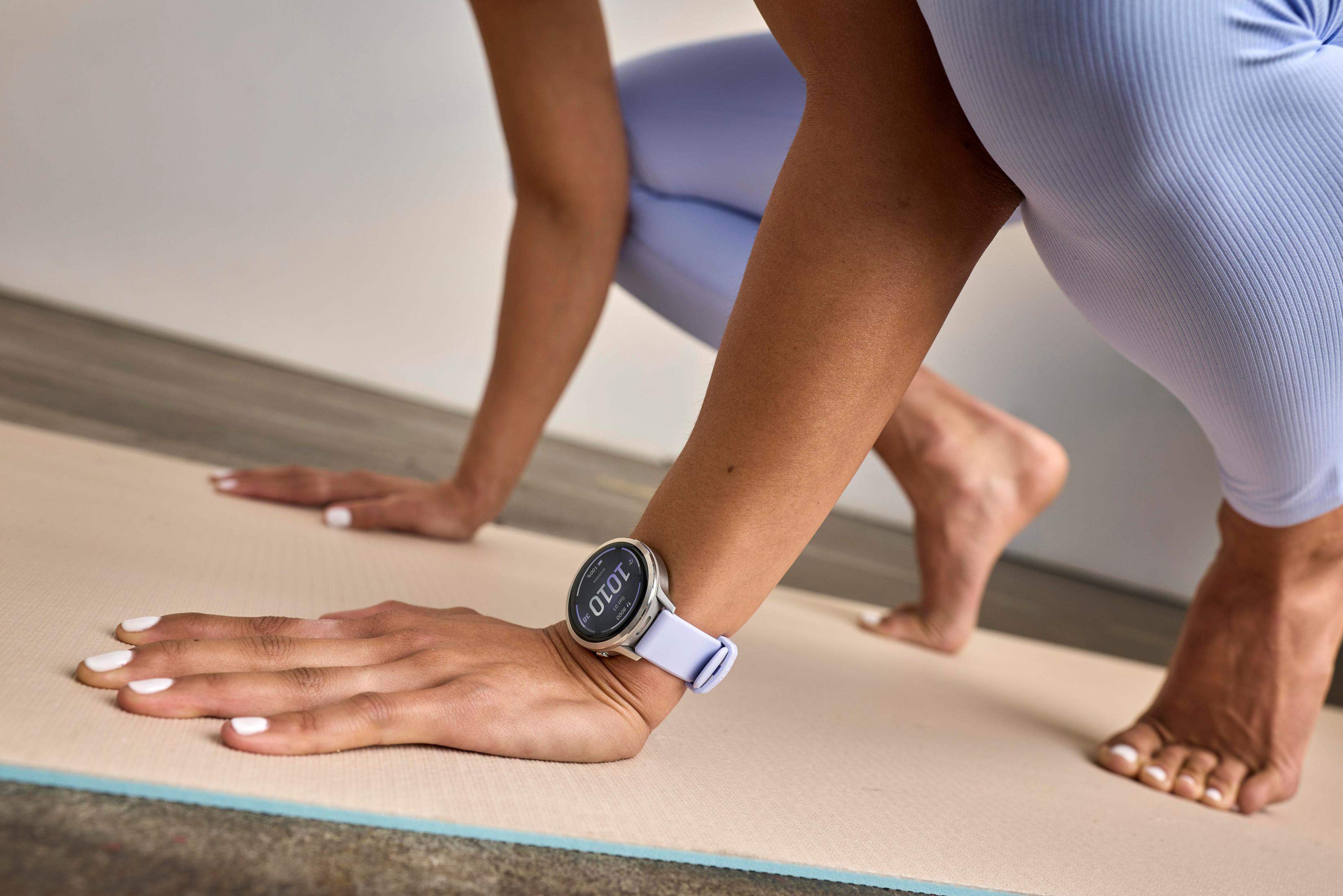 Personen in lila Kleidung auf einer Matte, Hände gestreckt, eine trägt eine Smartwatch.
