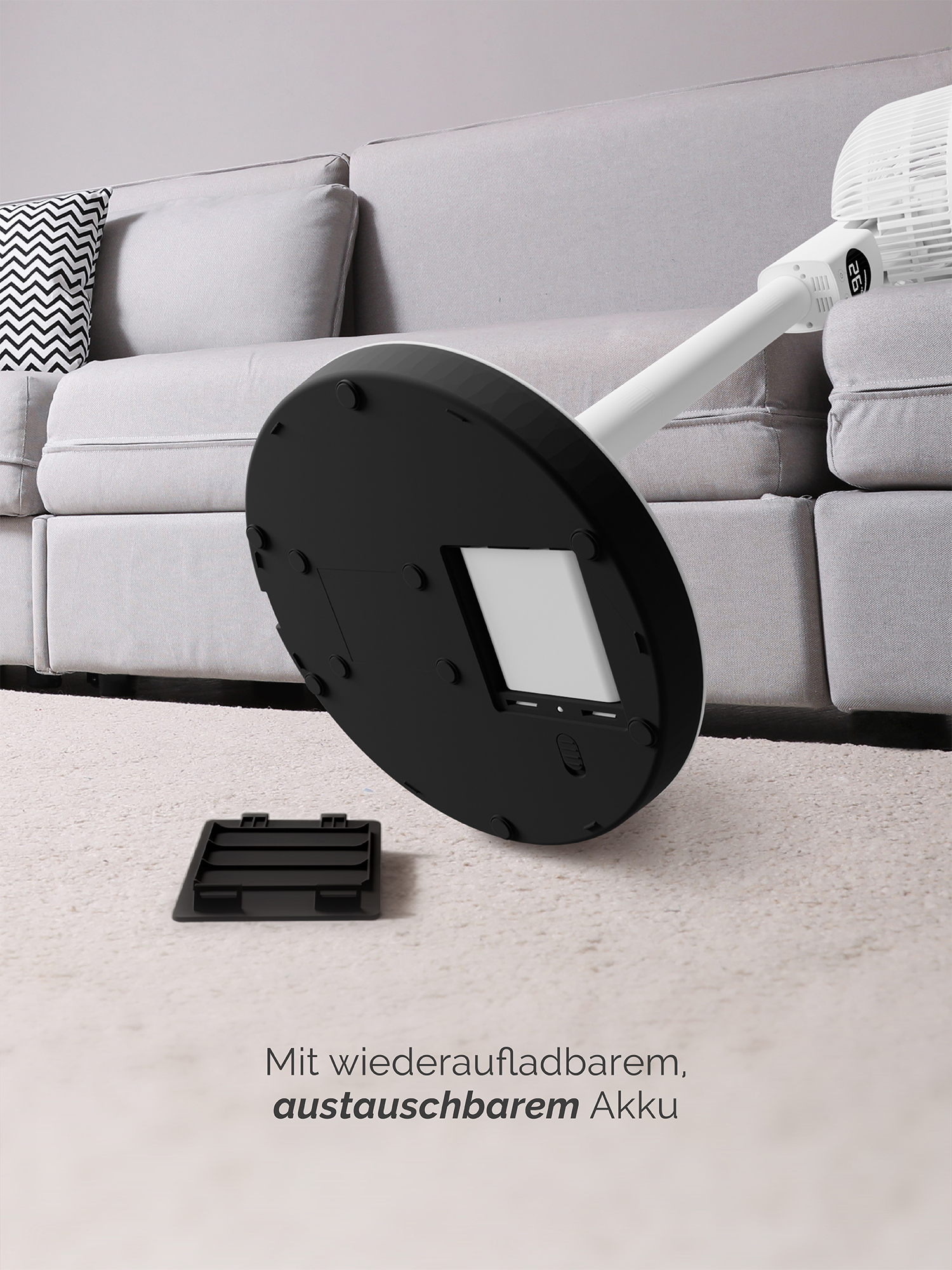 Un ventilatore bianco con base nera si trova su un tappeto chiaro accanto a un divano.