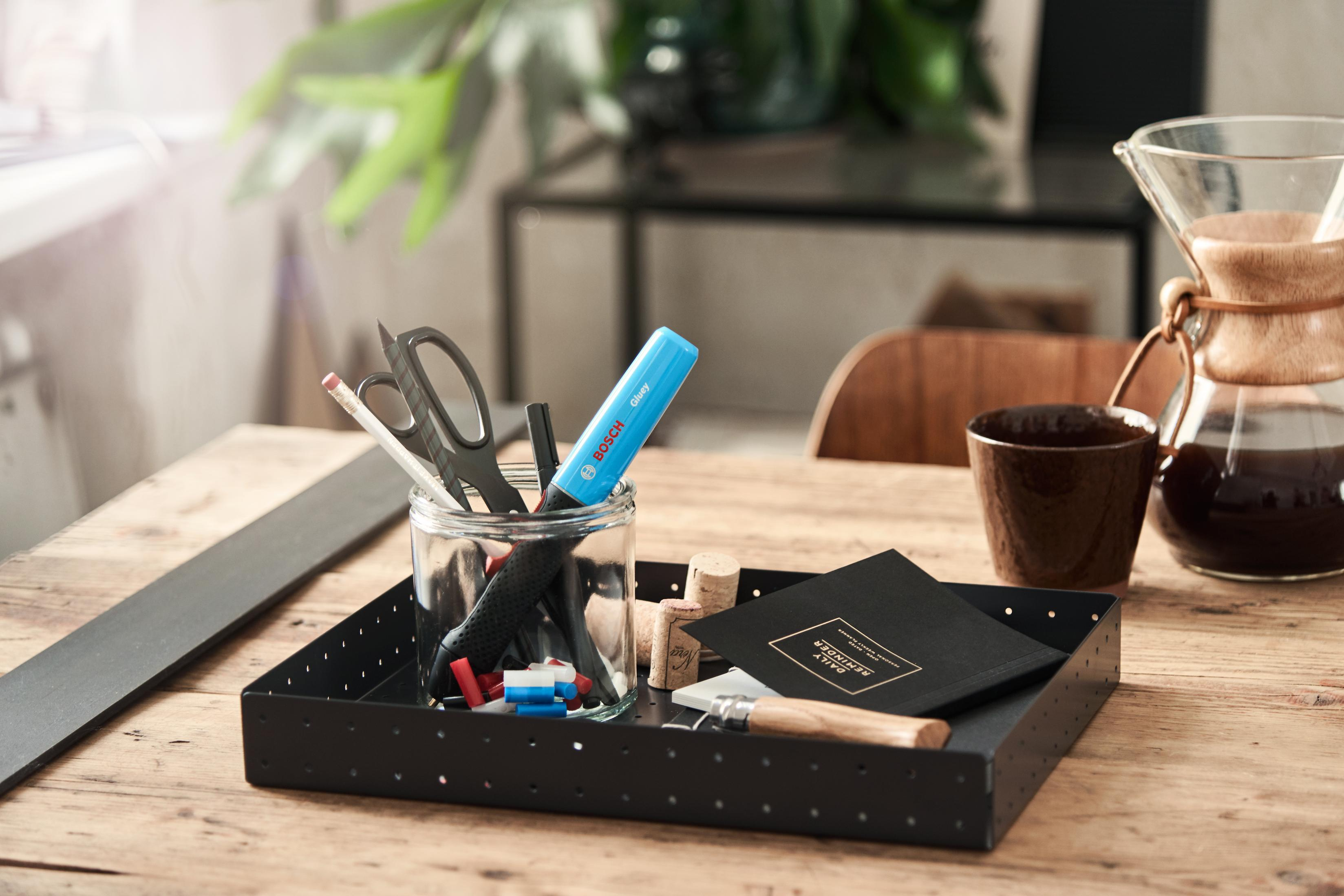 Schreibtisch mit Stiften, Schere, Kaffee und Notizbuch.
