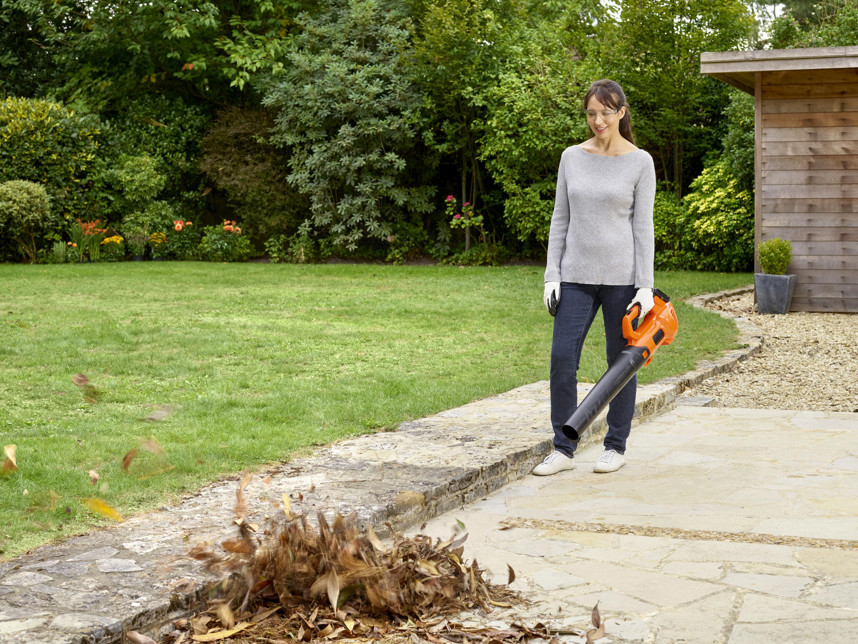 Donna soffia foglie con un soffiatore nel giardino.