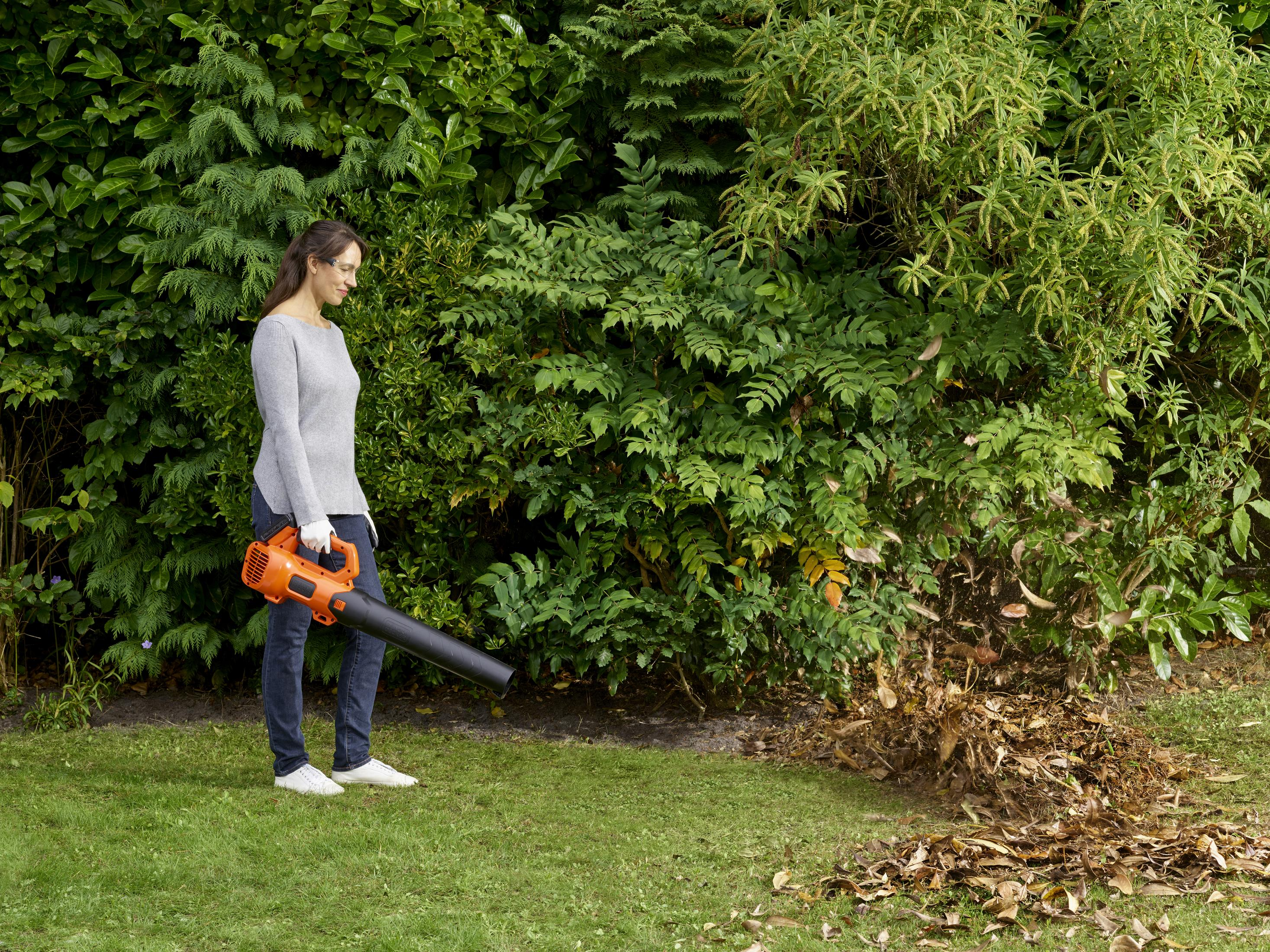 Donna con soffiatore per foglie in giardino, raccoglie foglie.