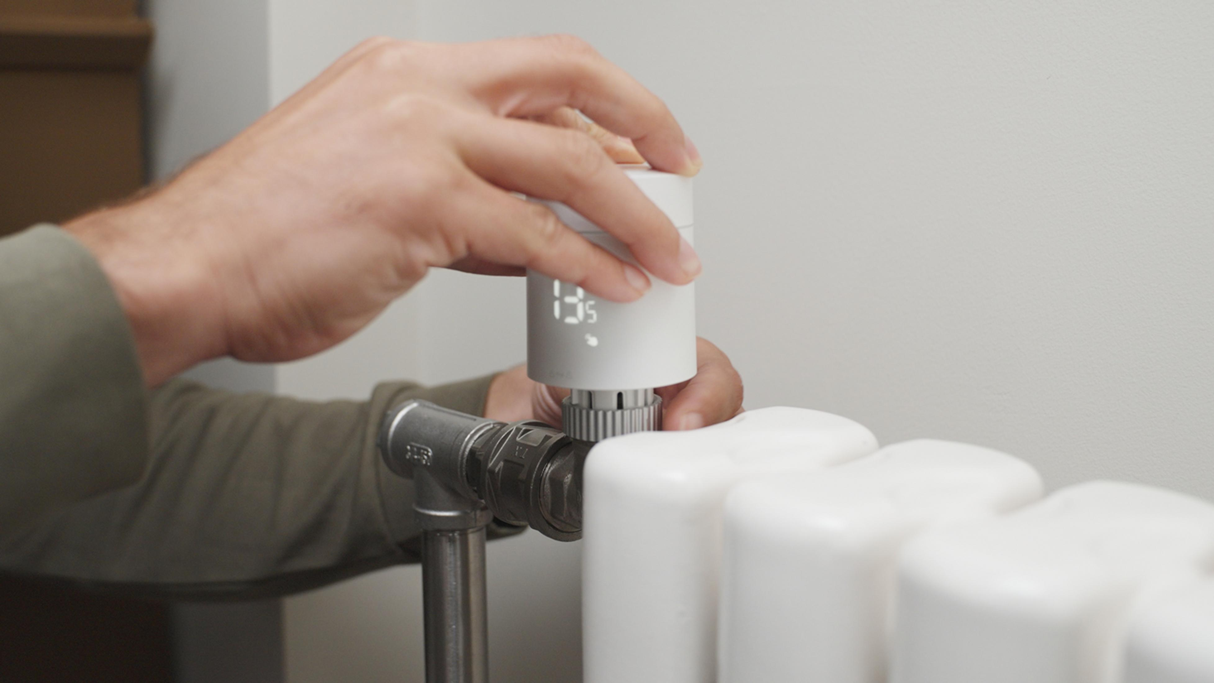 Mann dreht an einem weißen Heizkörperthermostat mit digitaler Anzeige.