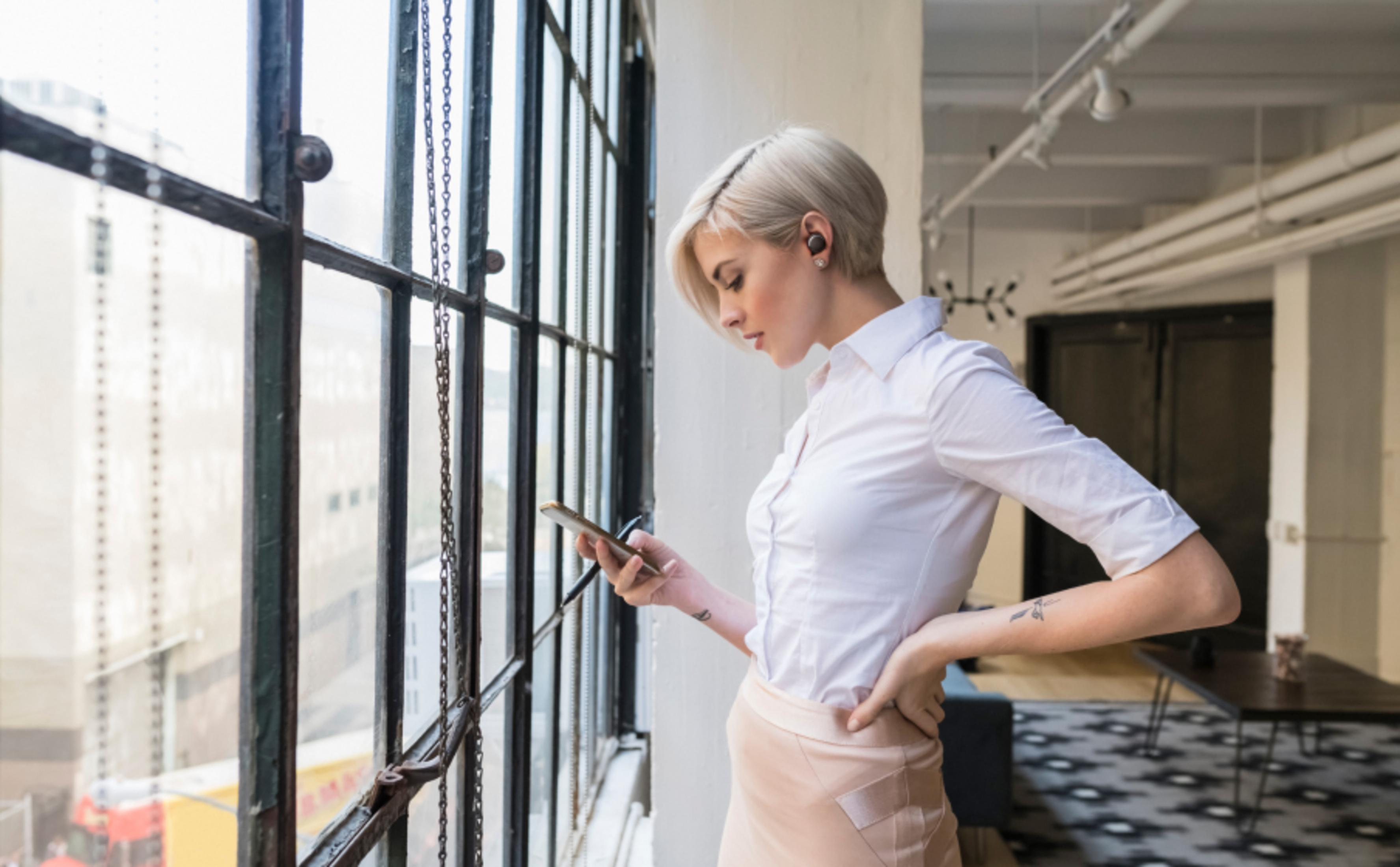 Una donna con i capelli biondi corti guarda il suo telefono che tiene in mano.