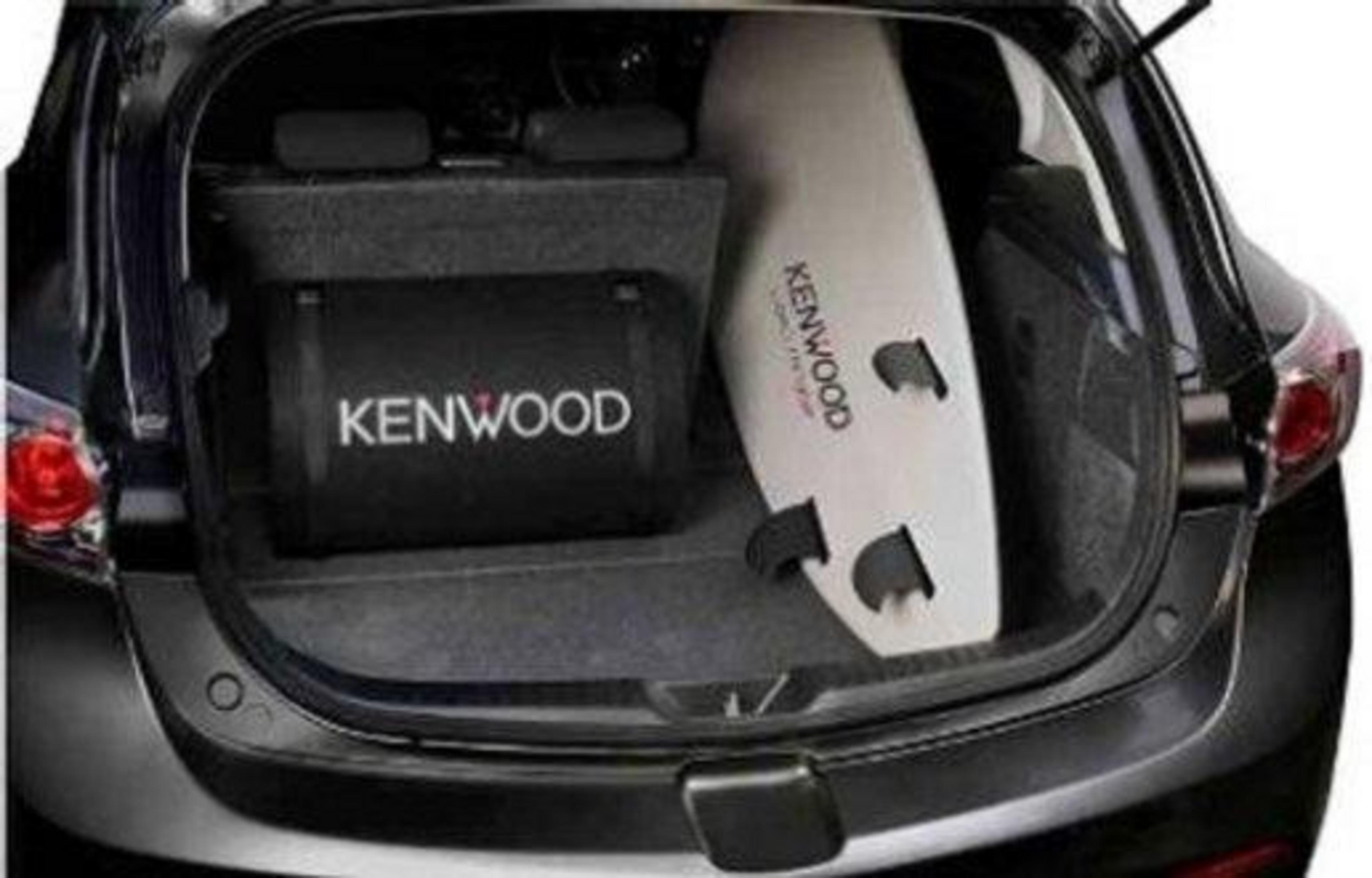 Ein weißes Surfbrett und ein Kenwood-Subwoofer liegen im Kofferraum eines Autos.