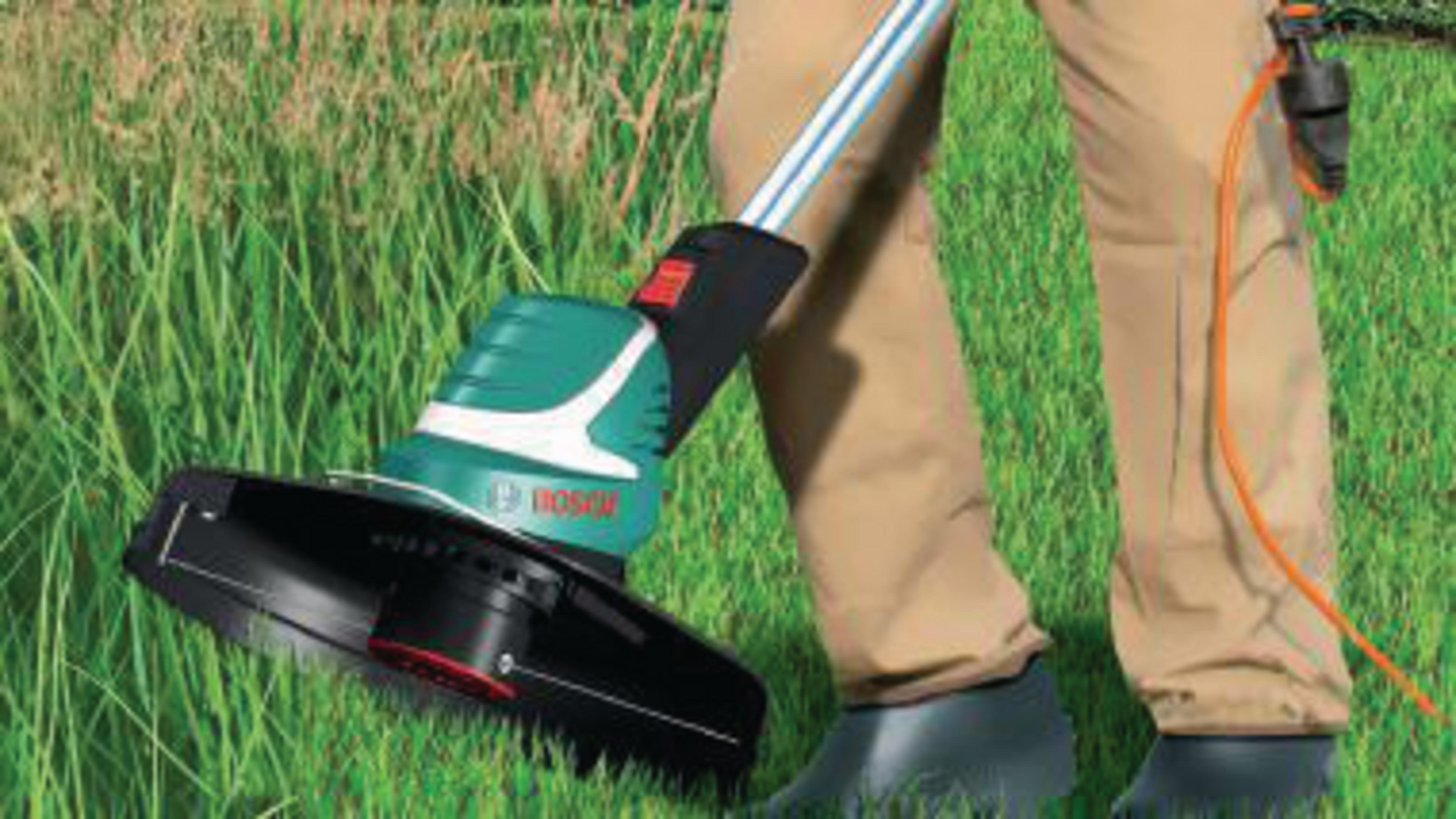 Grüner Bosch Rasentrimmer mit orangefarbenem Kabel im Gras.