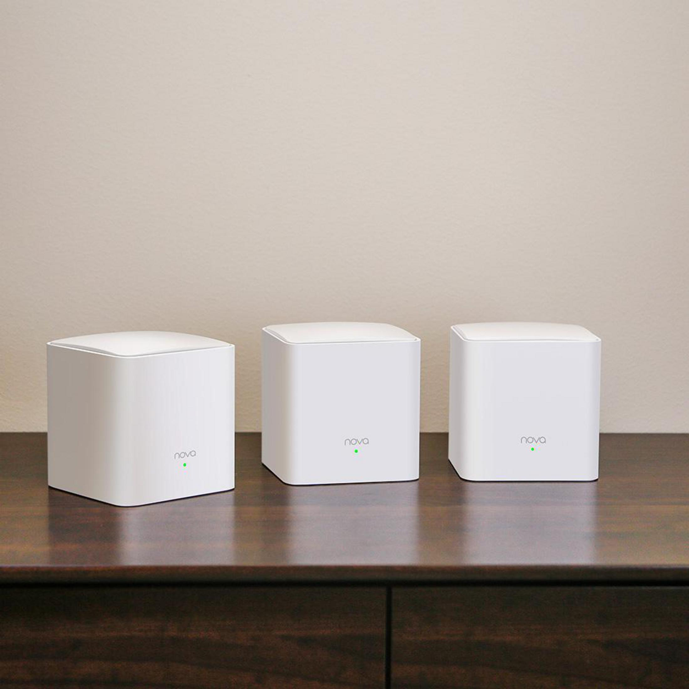 Tre router Wi-Fi bianchi, cubici, con LED verdi su un tavolo di legno scuro.