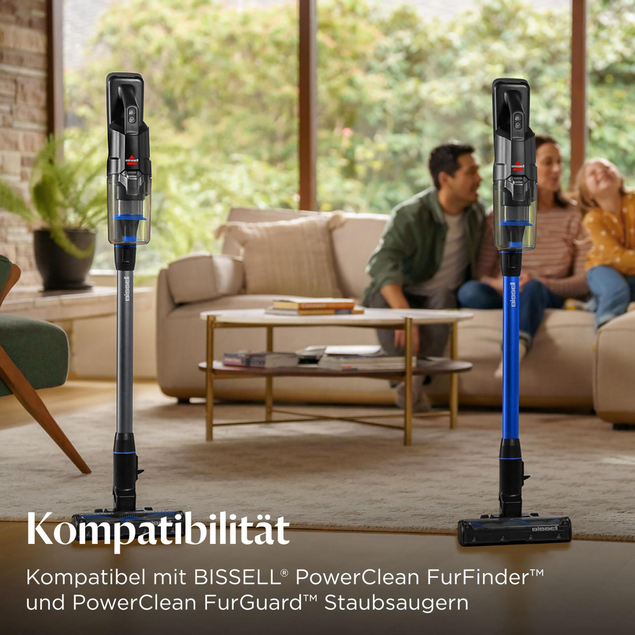 Zwei BISSELL Staubsauger stehen im Wohnzimmer, Familie sitzt im Hintergrund.