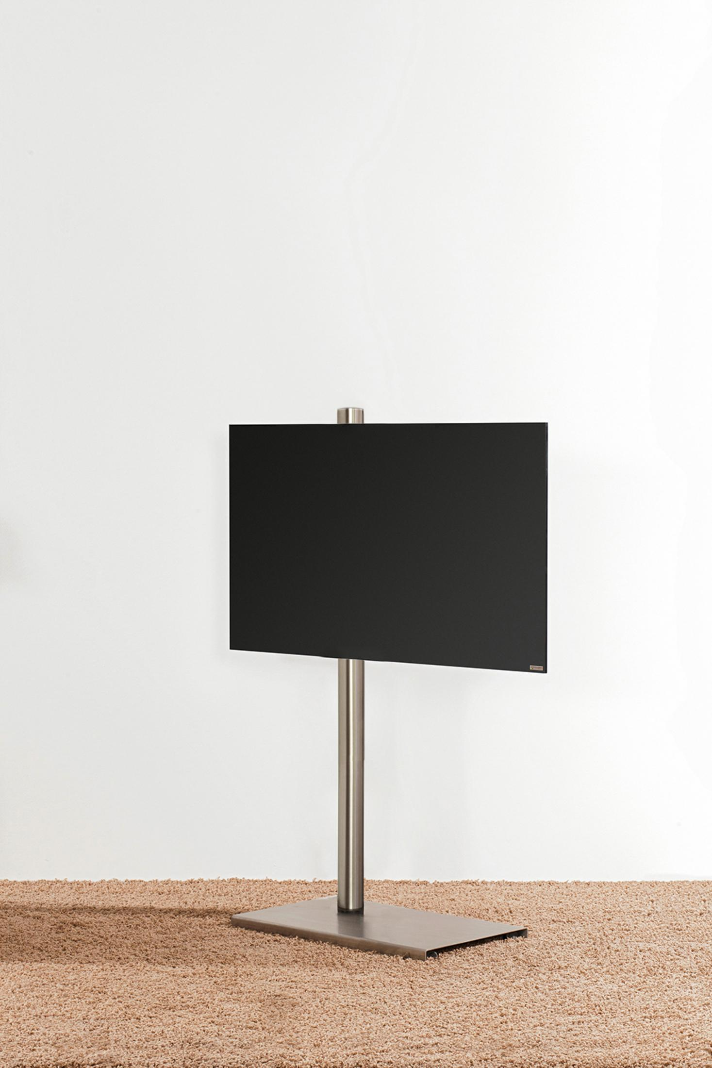 Ein schwarzer Fernseher auf einem Metallständer vor einer weißen Wand auf einem Teppich.