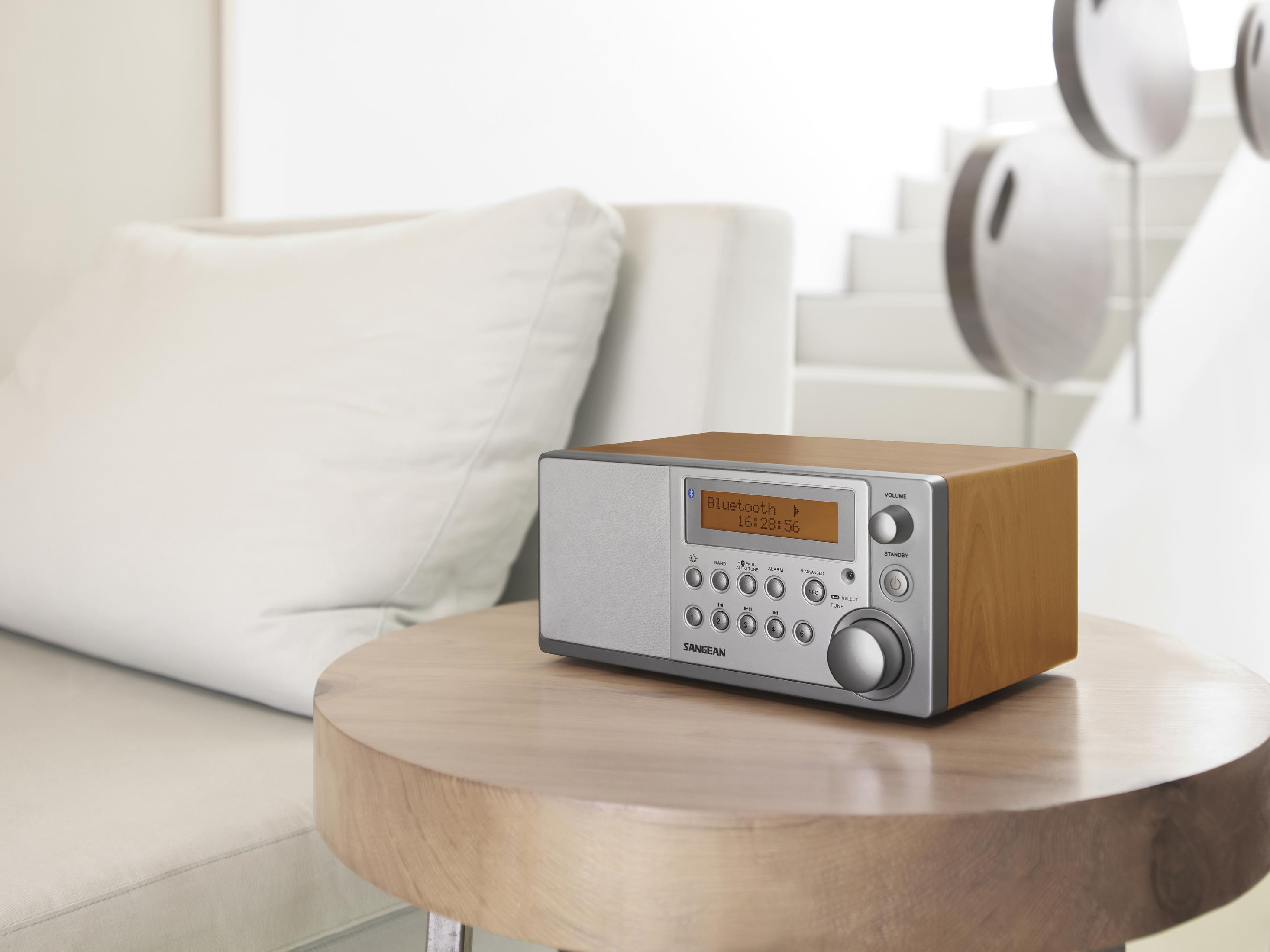 Ein Sangean Radio mit Holzgehäuse steht auf einem runden Holztisch neben einem Sofa.