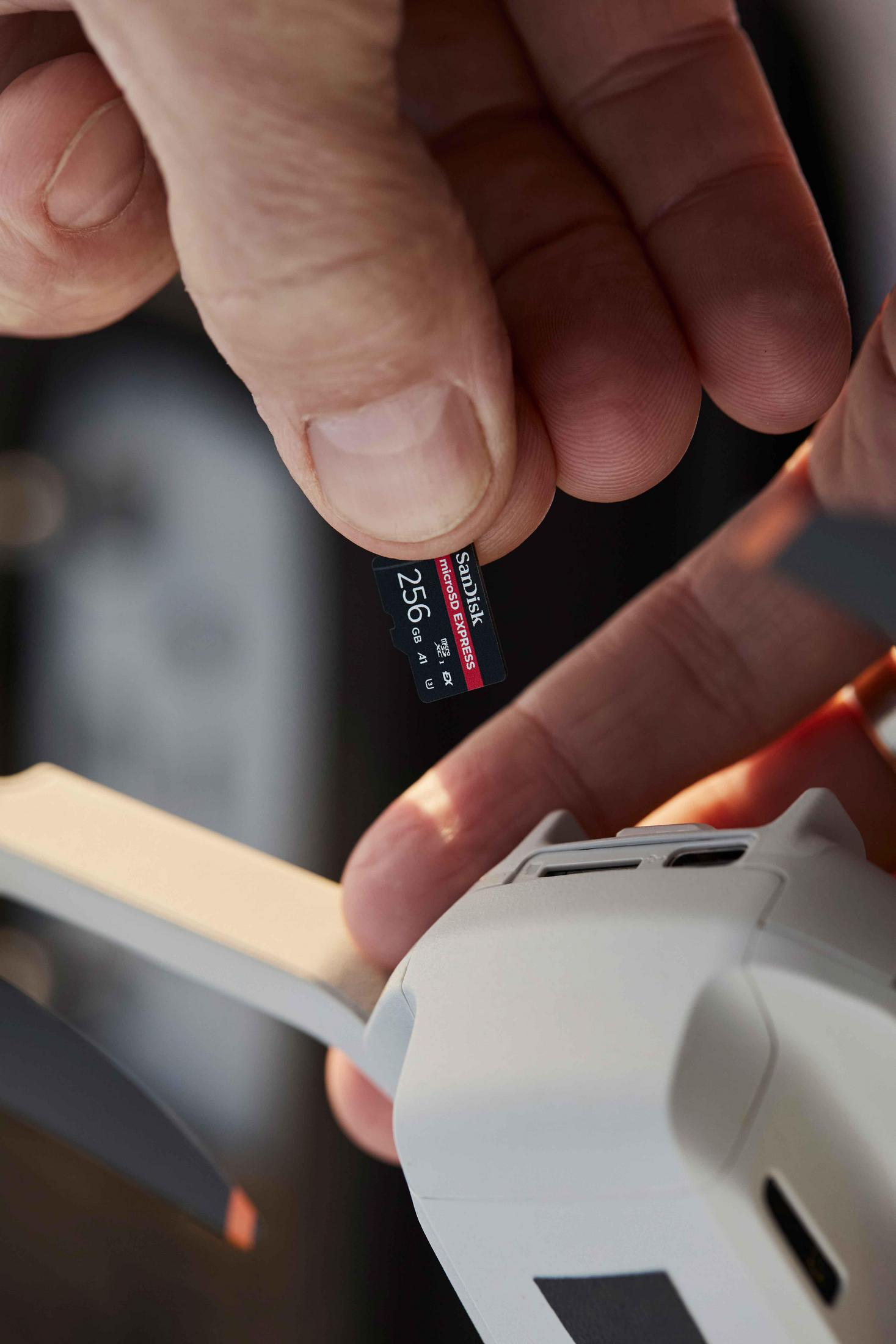 Una mano inserta una tarjeta microSD SanDisk de 256 GB en un dron blanco.