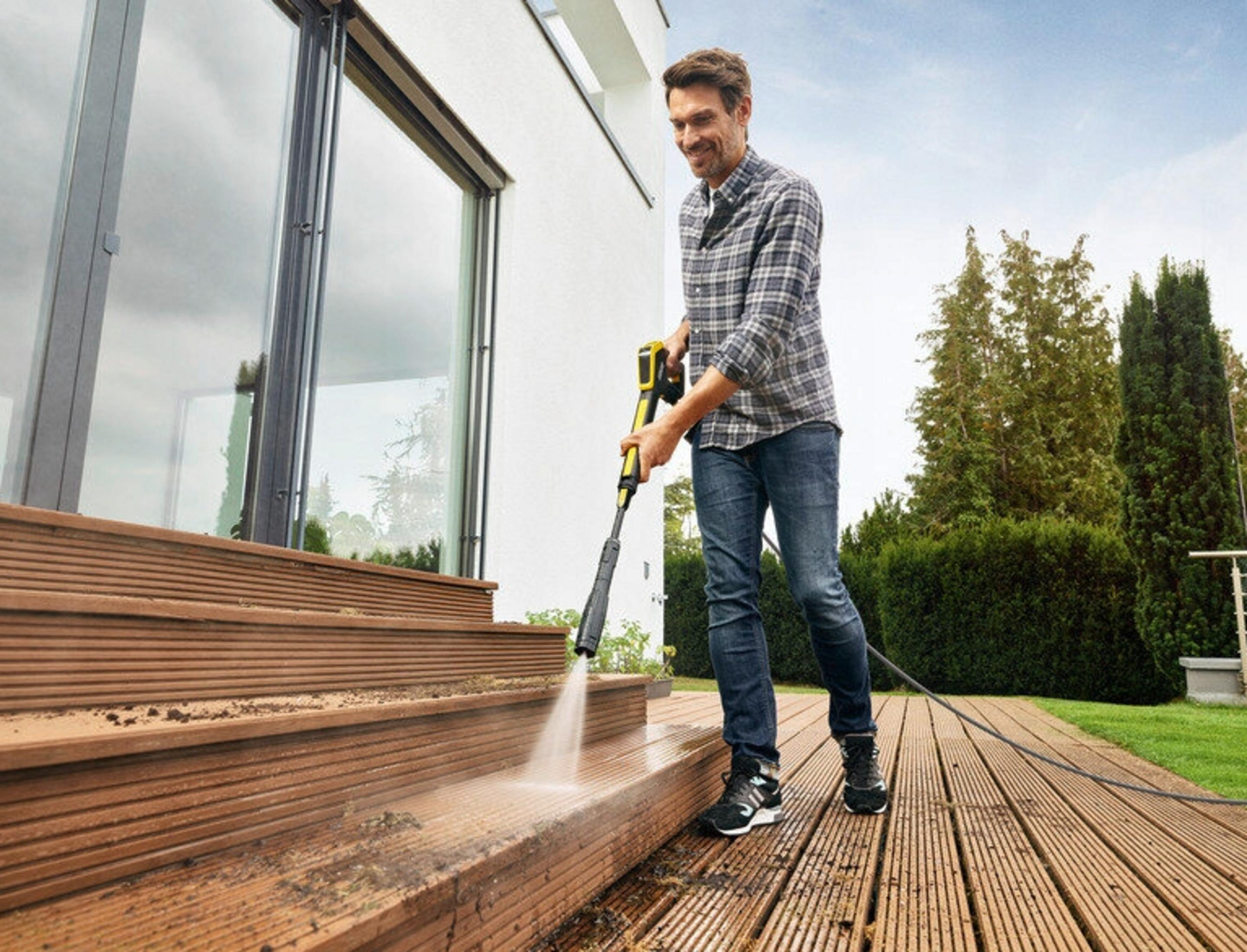 Uomo pulisce scale in legno con idropulitrice all'aperto.