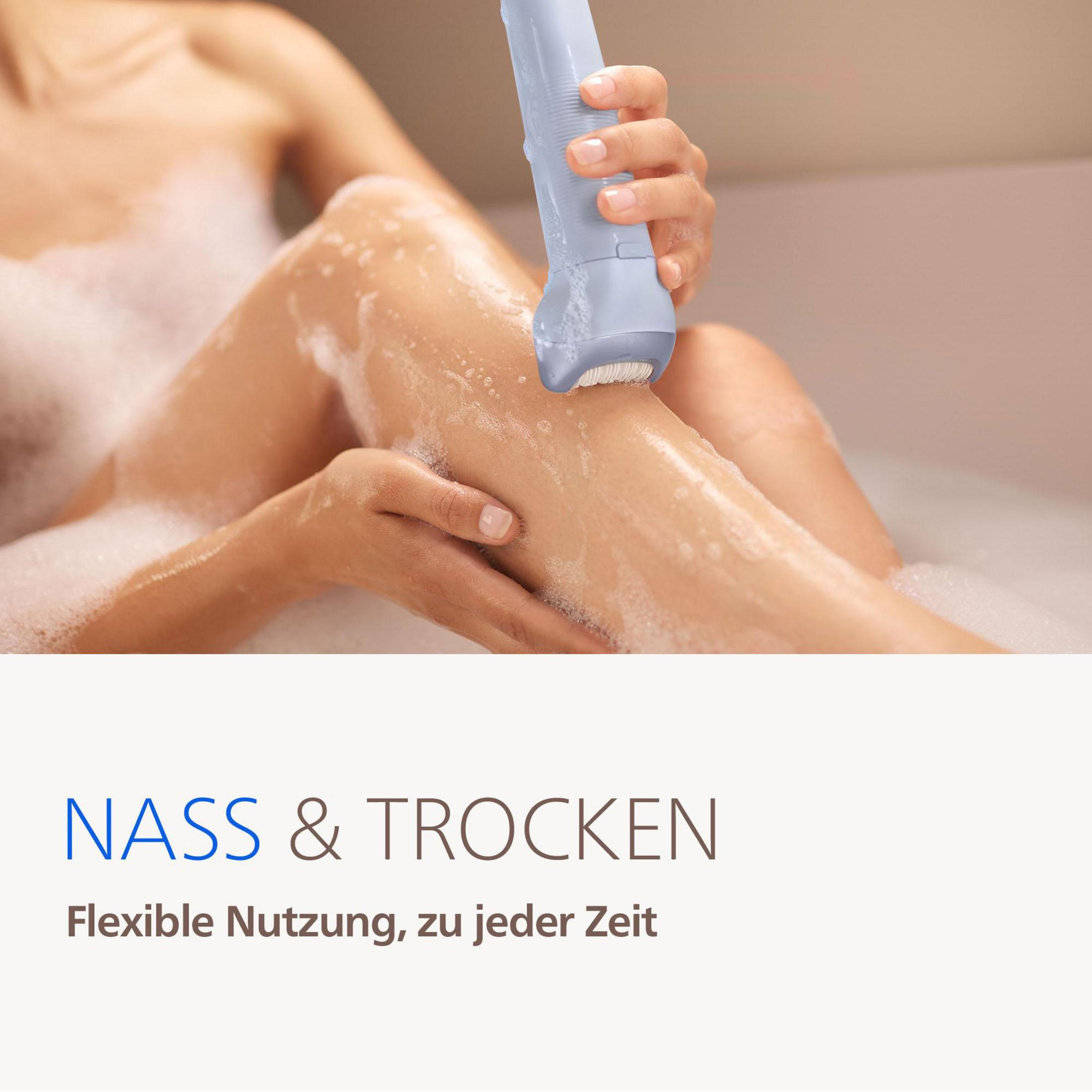 Eine Frau rasiert ihr Bein mit einem elektrischen Rasierer in der Badewanne mit Schaum.