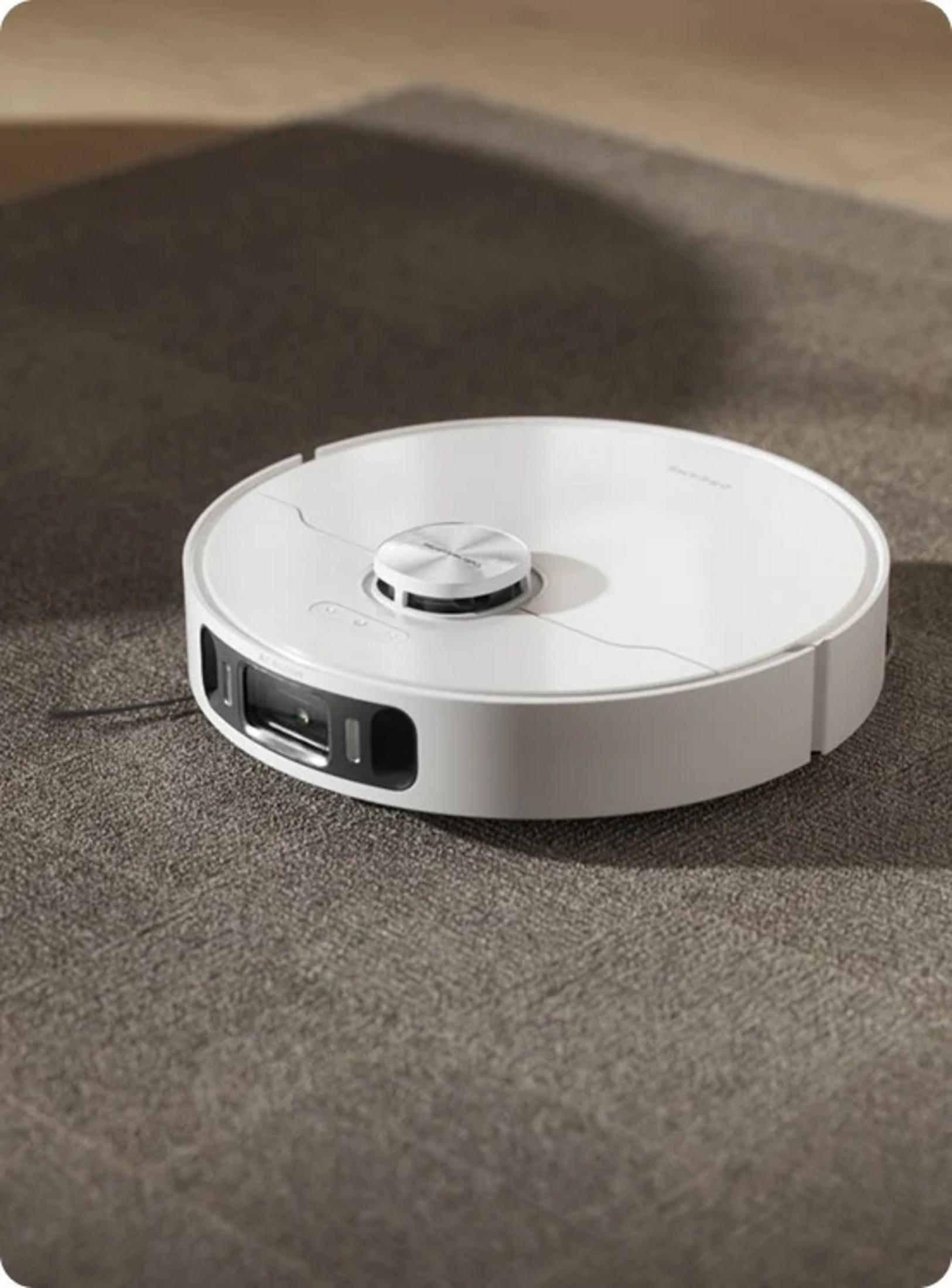 Un robot aspirapolvere bianco su un tappeto grigio con ombre sullo sfondo.