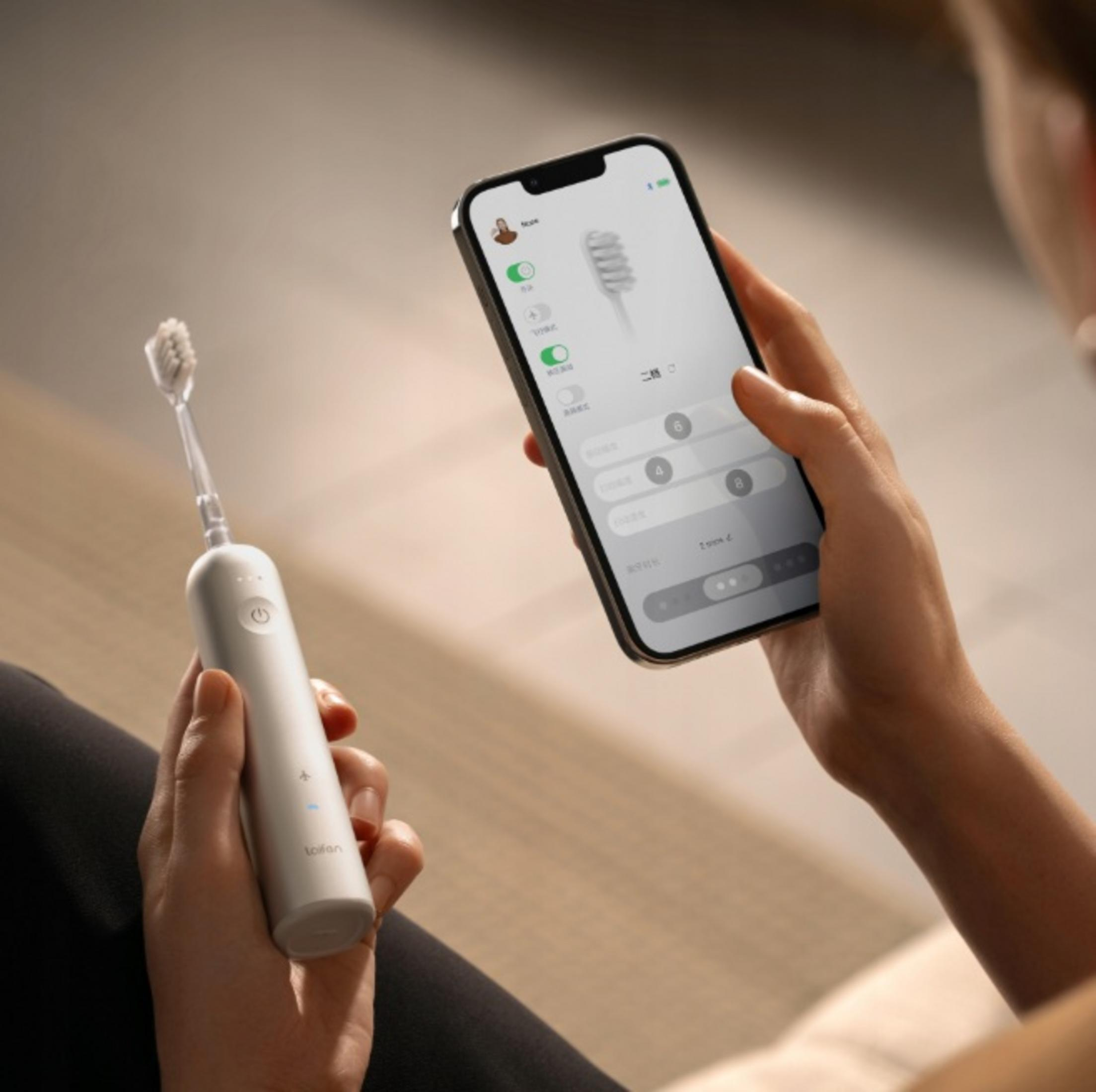 Bir kişi, bir uygulama arayüzü gösteren beyaz elektrikli diş fırçası ve akıllı telefon tutuyor.