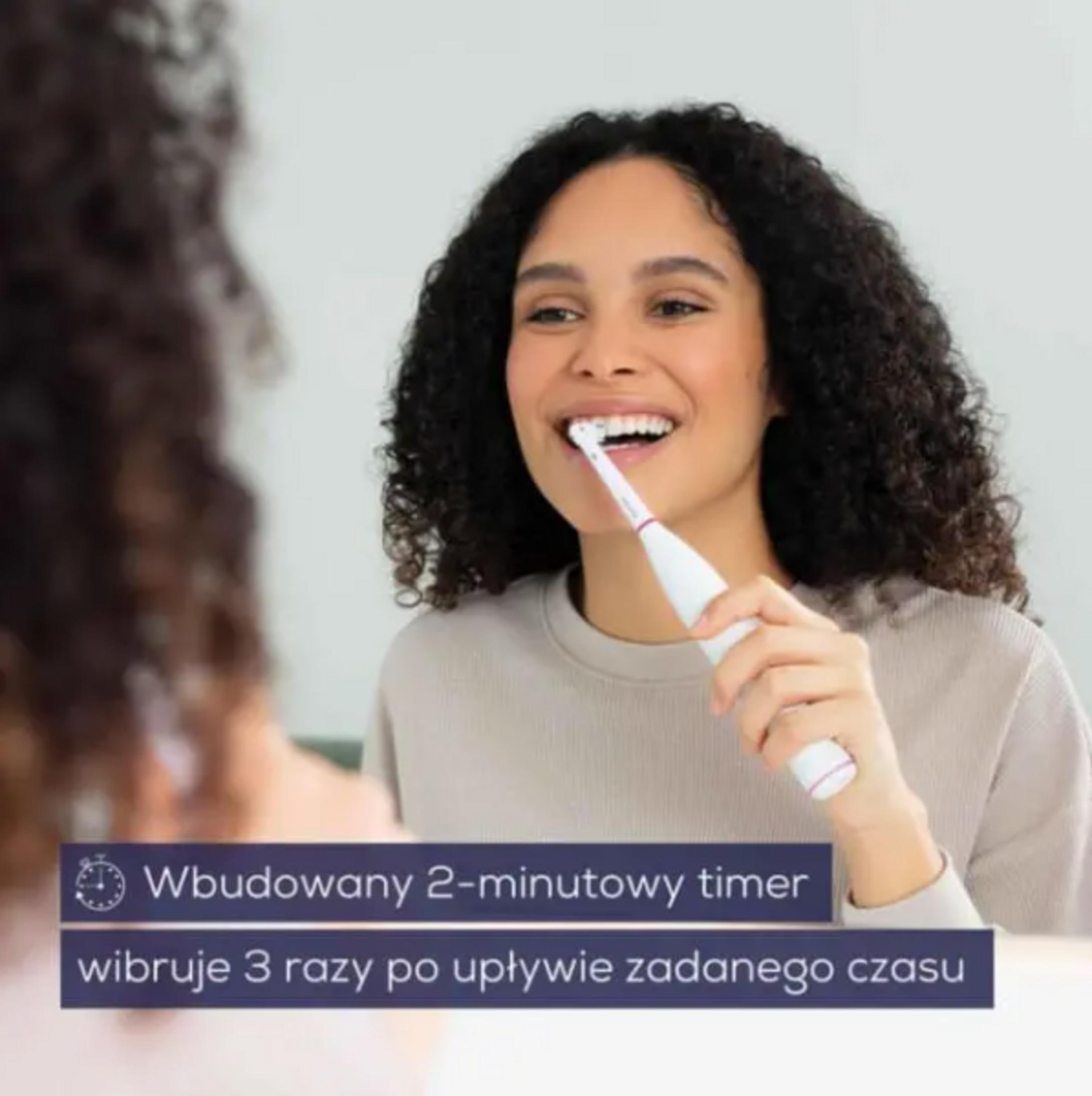 Une femme se brosse les dents avec une brosse à dents électrique.