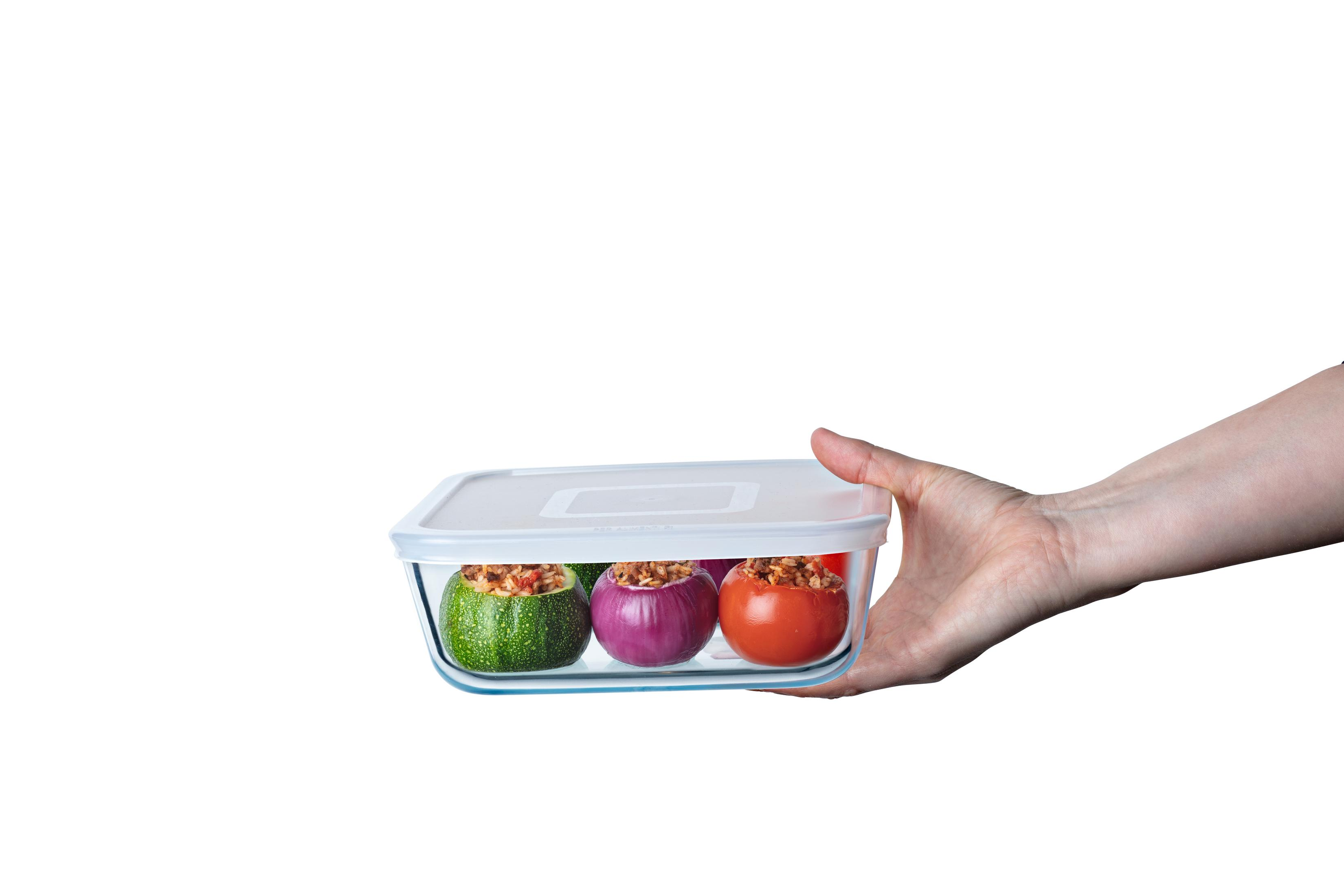 Mano che tiene contenitore in vetro con zucchine, cipolla e pomodoro ripieni.