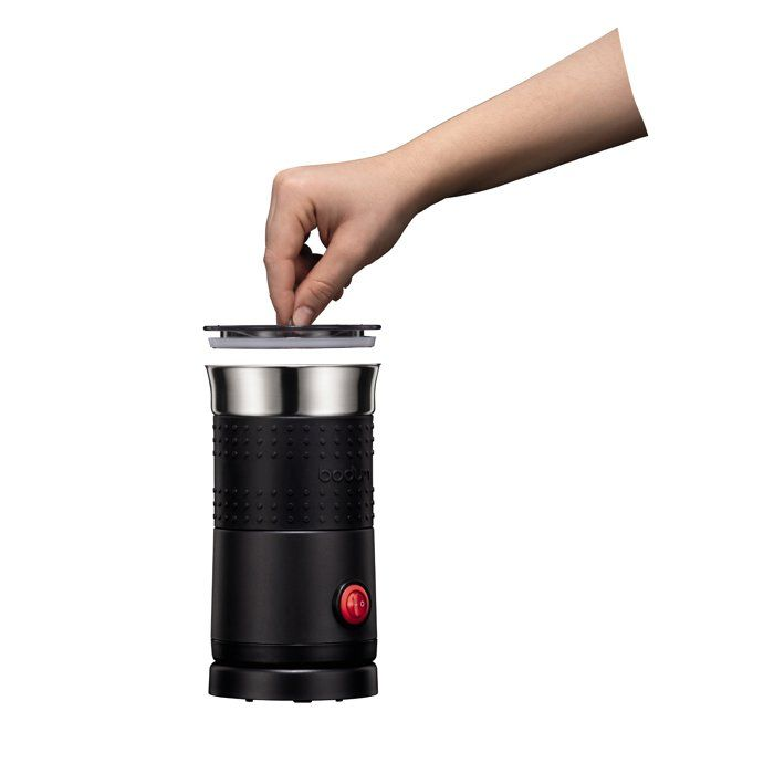 Una mano posa il coperchio su uno spumatore di latte nero con pulsante rosso.