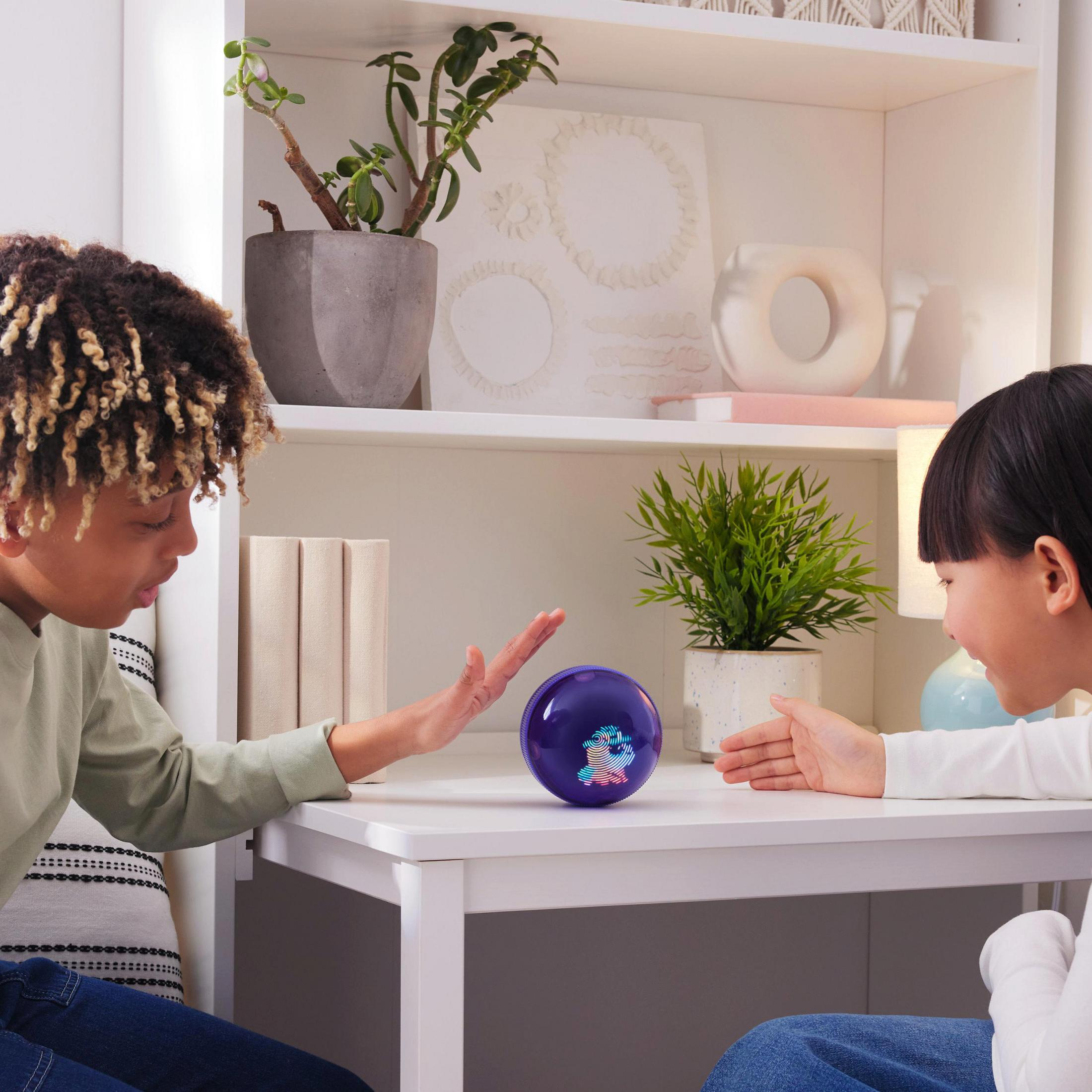 Due bambini giocano con una palla viola luminosa su un tavolo bianco.