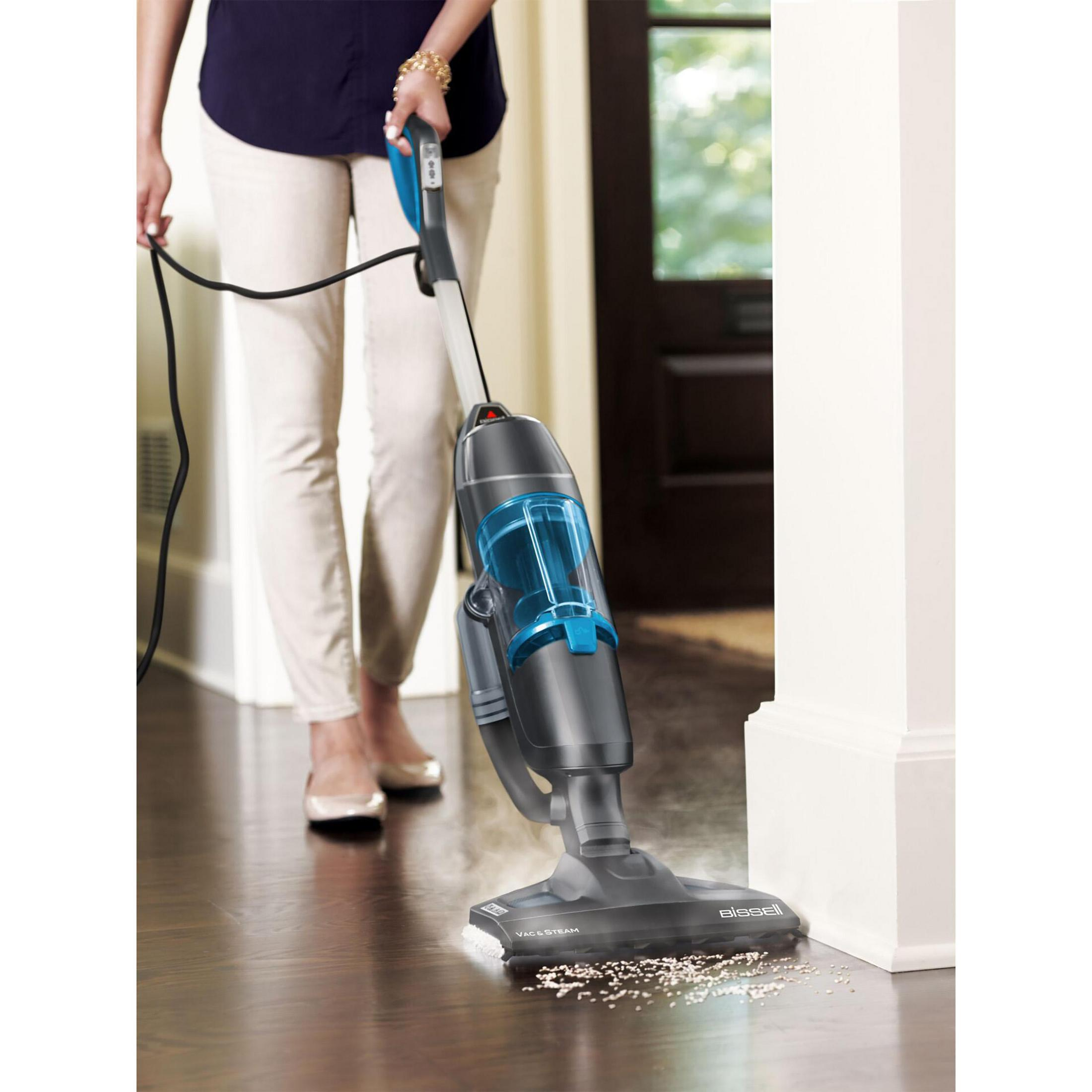 Una persona aspira sporco su un pavimento in legno con un aspirapolvere a vapore Bissell grigio e blu.