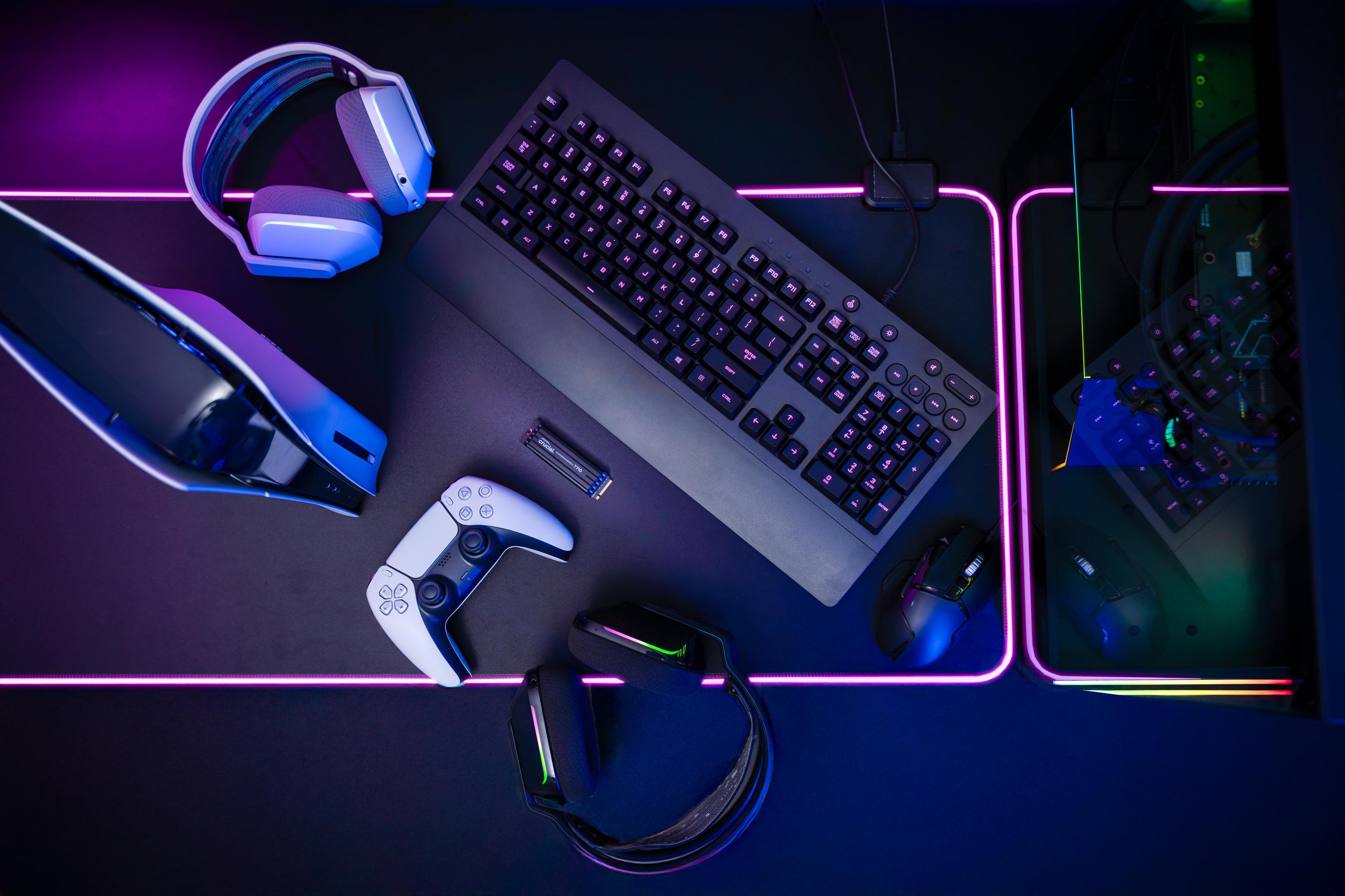 Setup da gioco con tastiera, mouse, controller, cuffie e console, illuminato da luce al neon.