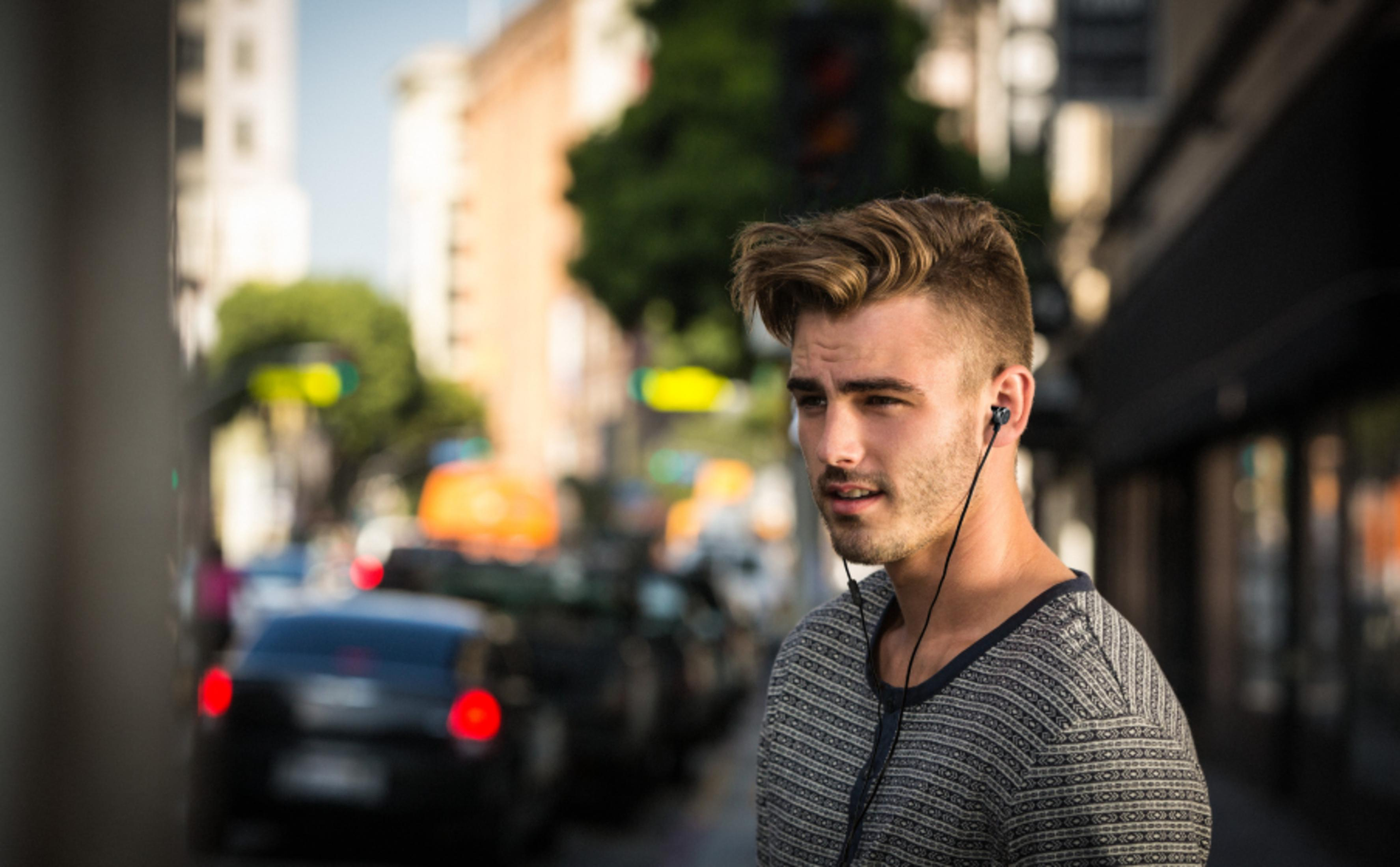 Un uomo con auricolari all'aperto, con auto ed edifici sfocati sullo sfondo.