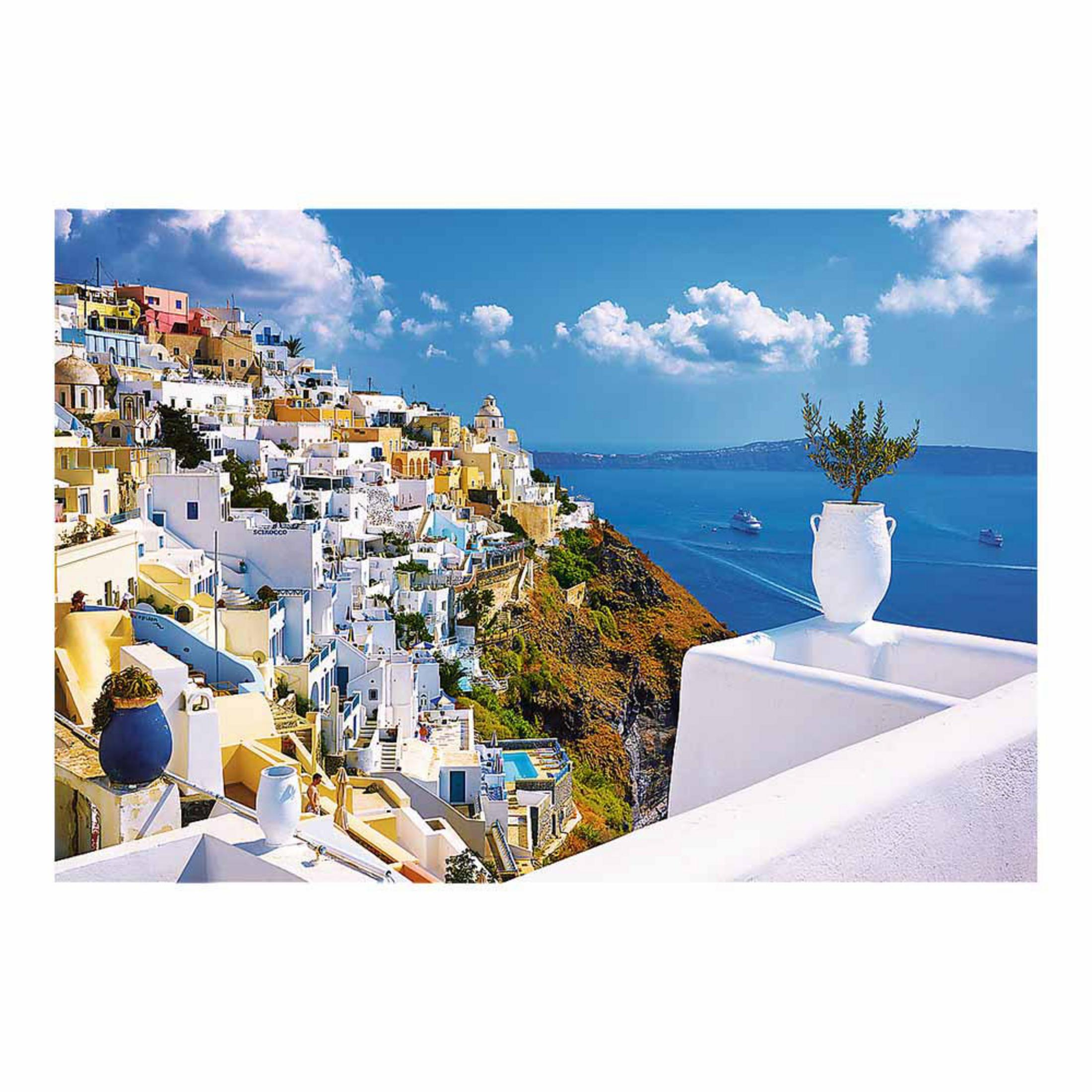 Casas blancas en una ladera con el mar azul y barcos al fondo.