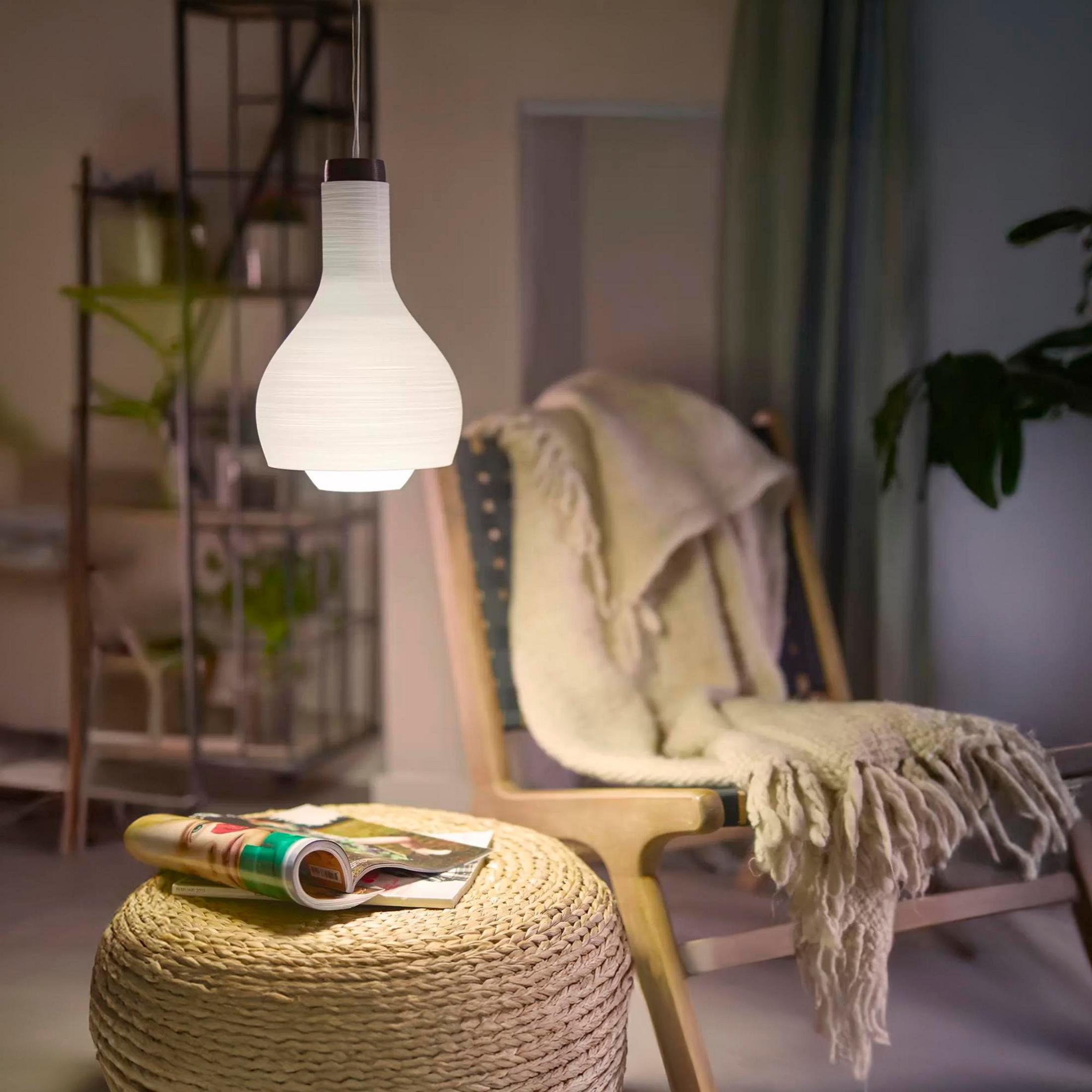 Un abat-jour suspendu blanc surplombe un pouf rond avec des magazines.