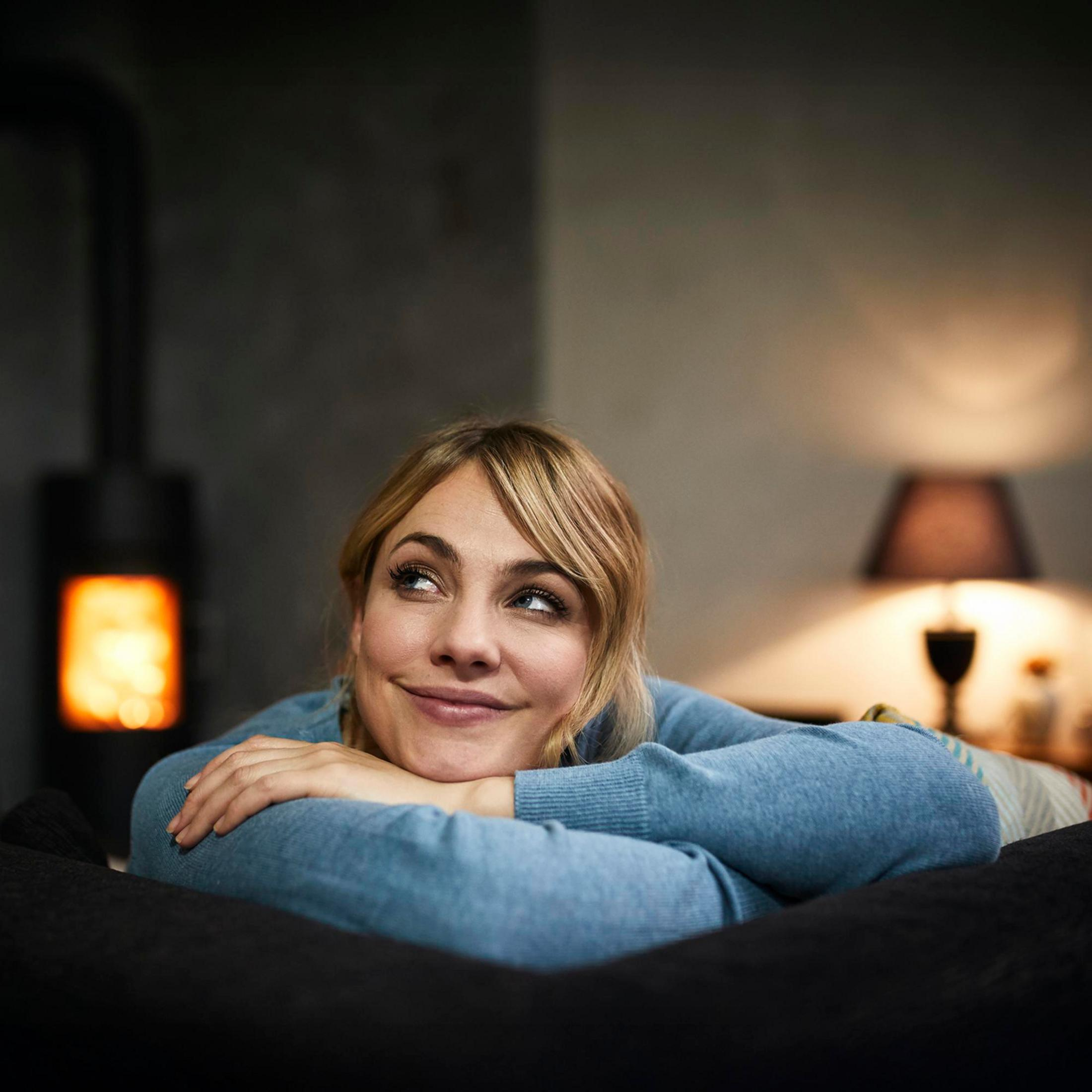 Une femme se repose sur un canapé devant une cheminée allumée.