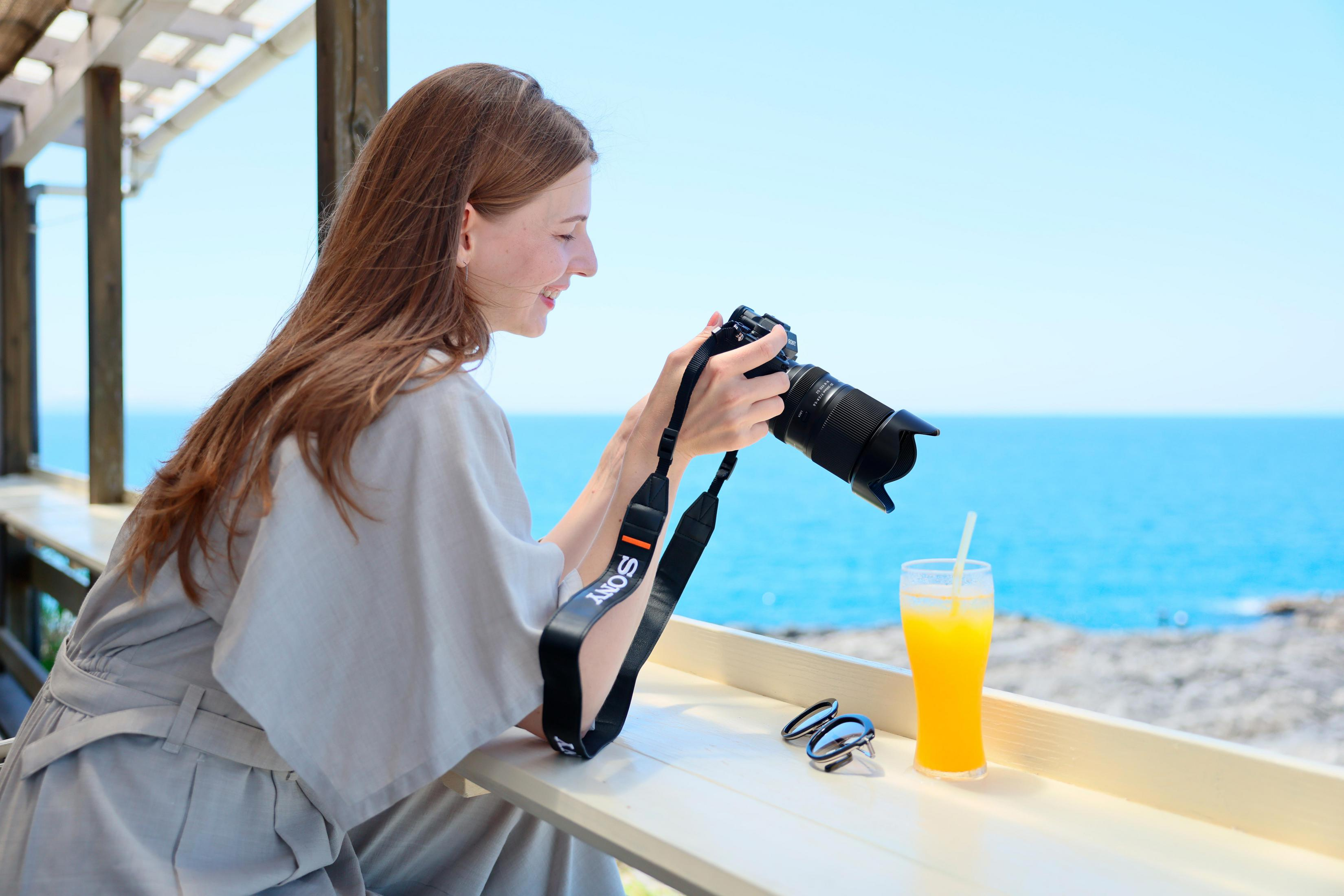 Frau mit Kamera und Orangensaft am Meer