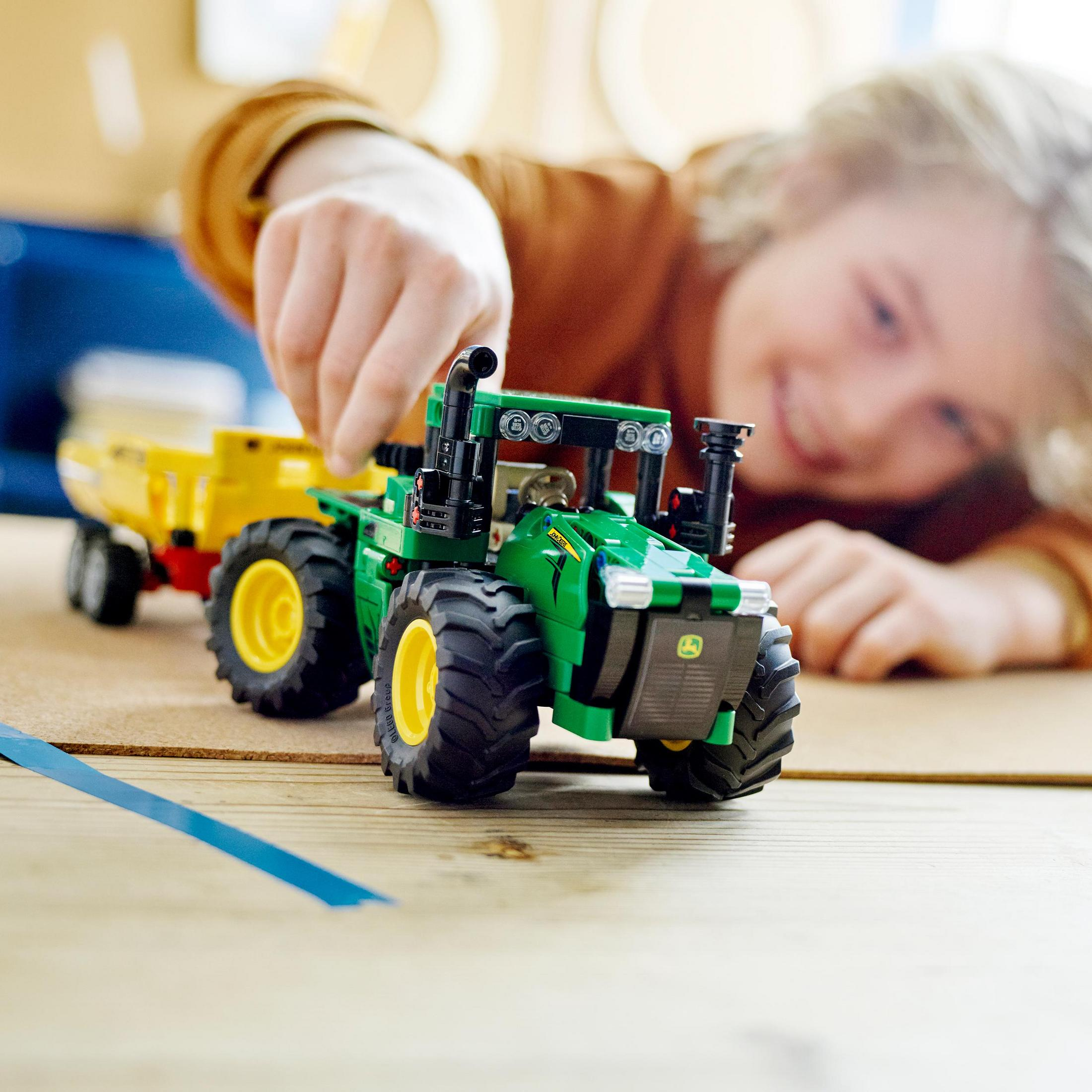 Grüner Spielzeugtraktor mit Anhänger, der von einem Kind auf einem Holztisch geschoben wird.