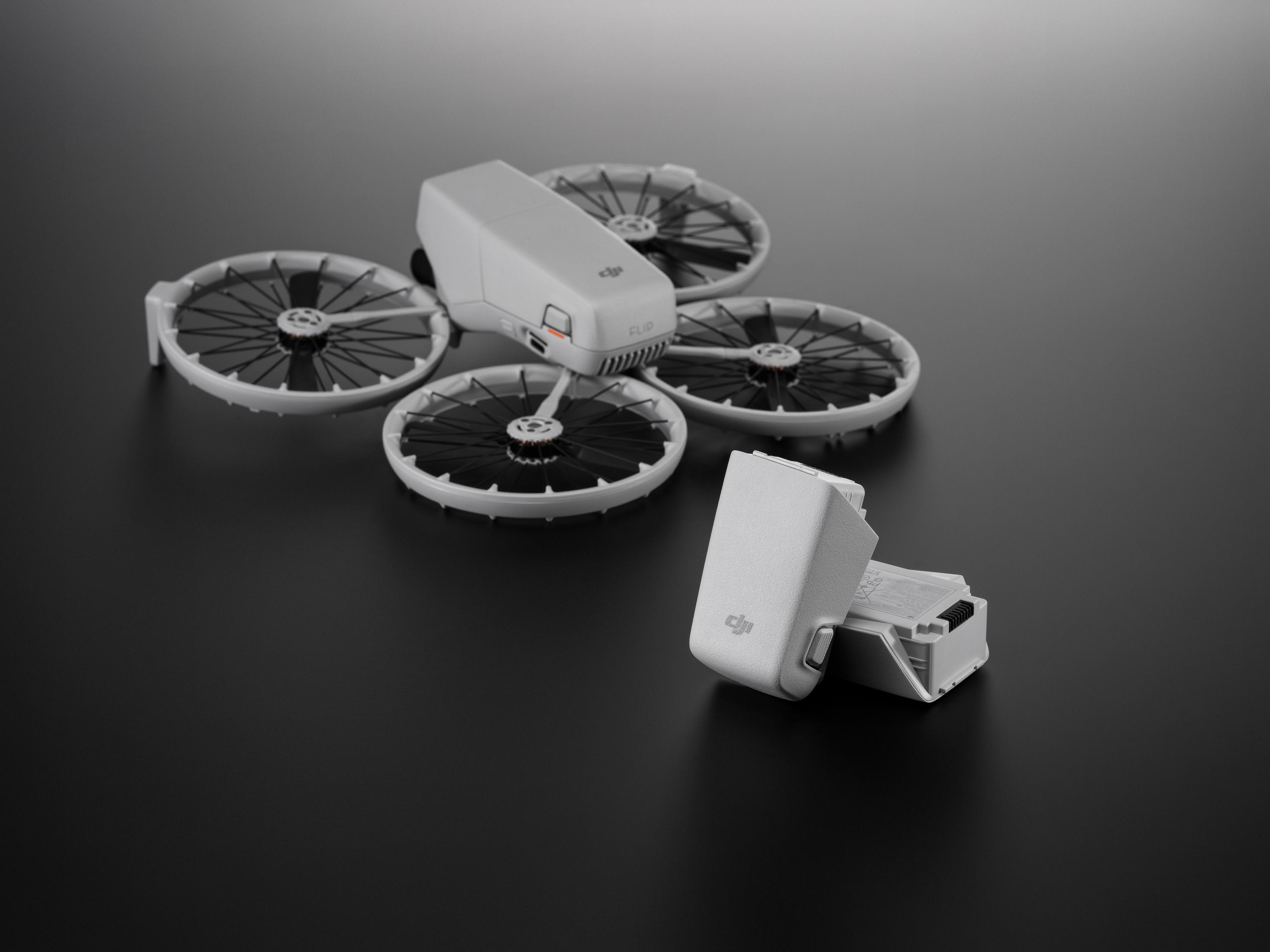 Un modello di drone bianco giace su una superficie scura, con una batteria accanto.